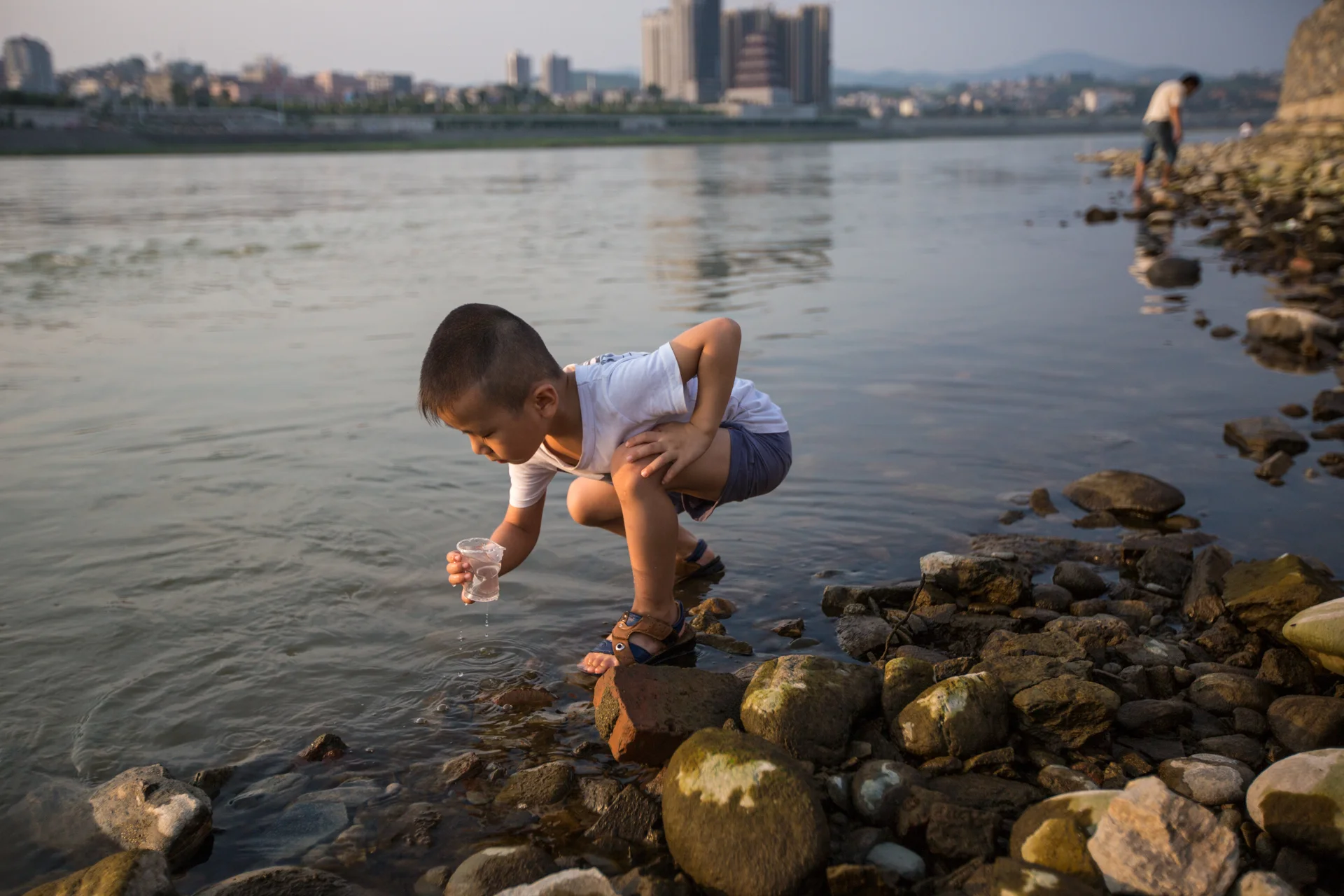  A boy on the Han River in Ankang on July 21, 2015, tries to catch fish in a plastic cup as he just watched his father (background) do. The Han River runs through Ankang from west to east and locals use it for swimming, fishing, boat transportation, 