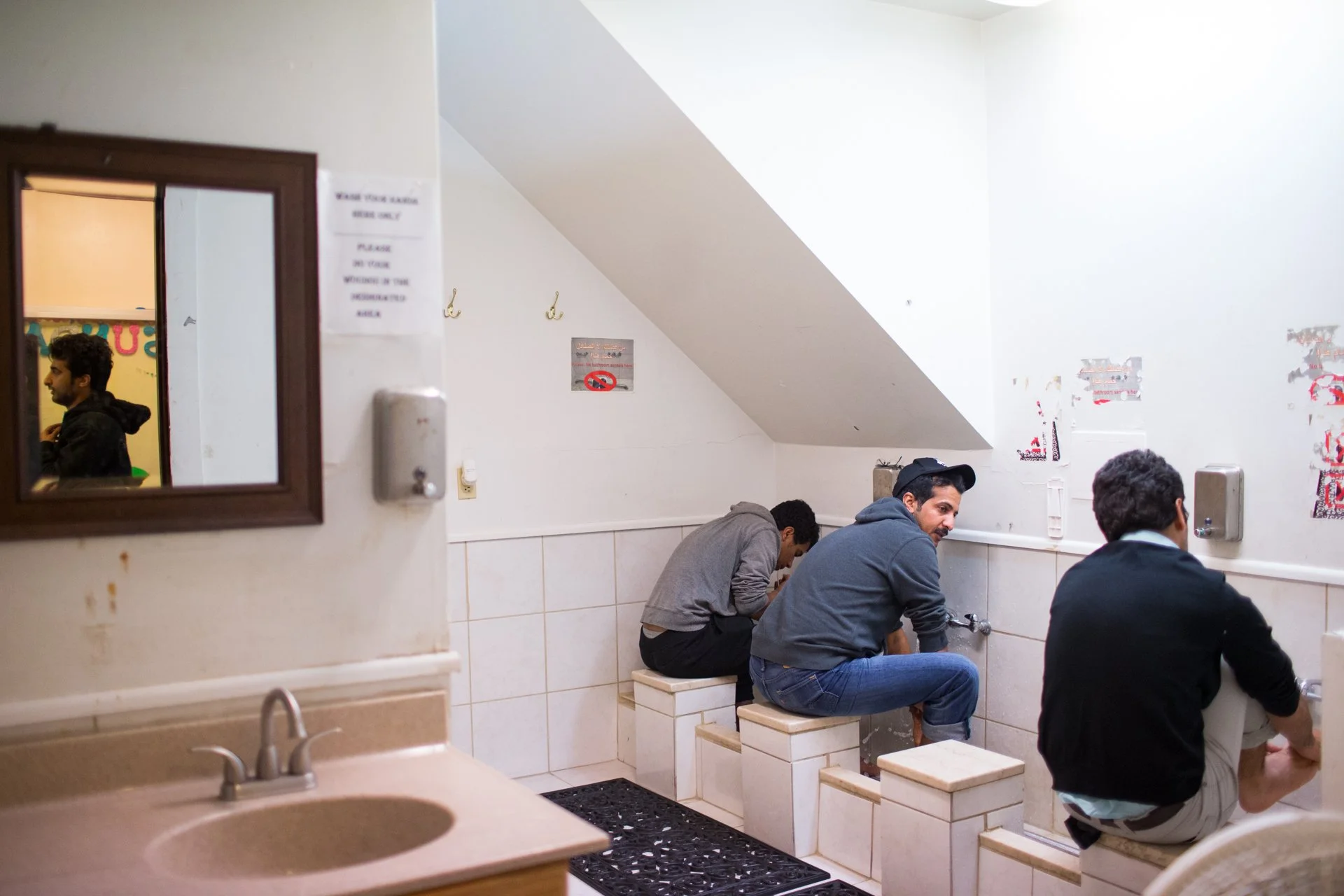  Abdullah Alkhusaibi (seated, left), Abdulrazaq Alanazi (middle), and Salmah Al-Khahtani make Woudu, a ritual washing mandatory before each prayer, while Muaath Dawadmi enters the service. The washing takes a few minutes and consists of washing the h