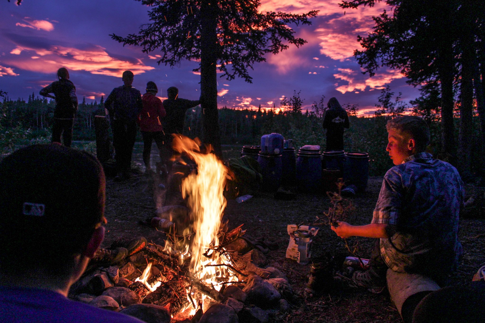  Group of campers sitting around fire at sunset 