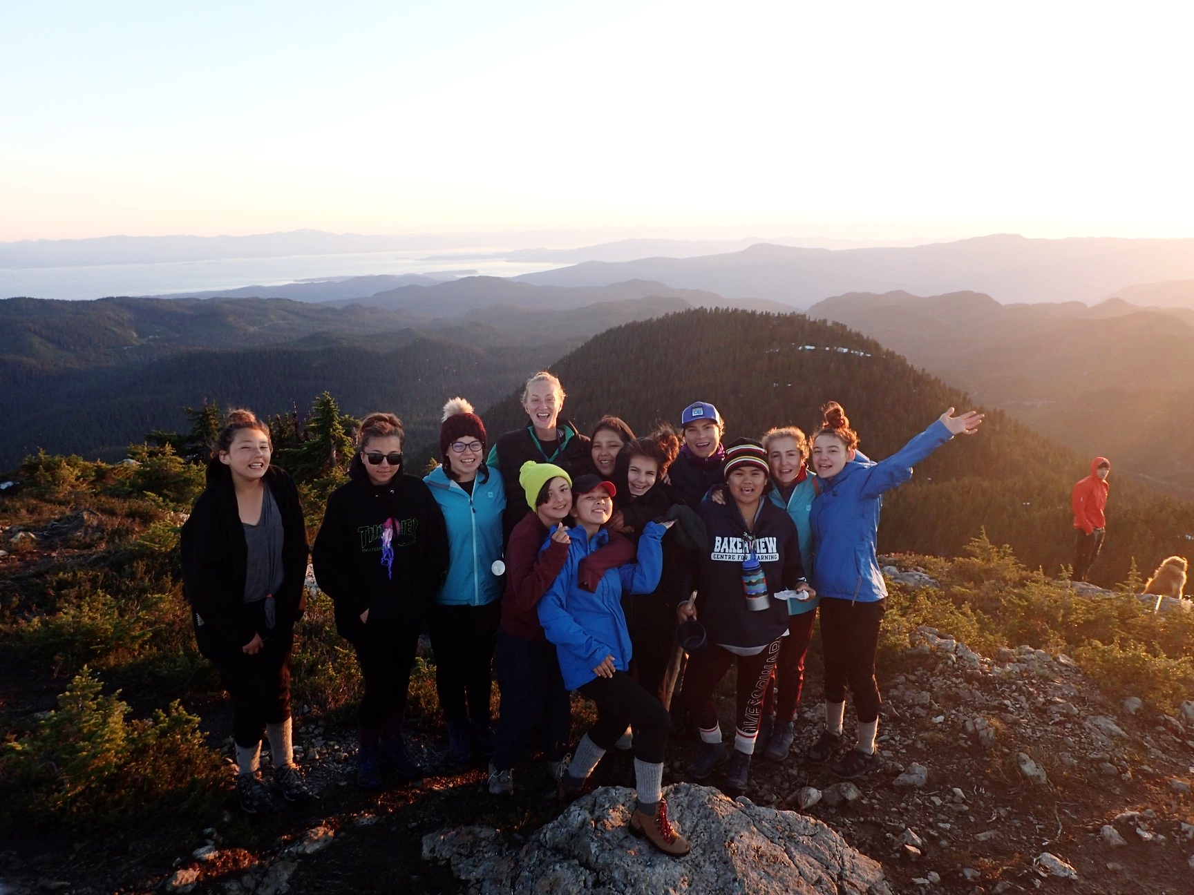  Group photo of 12 smiling teenage girls on mountaintop at sunset 