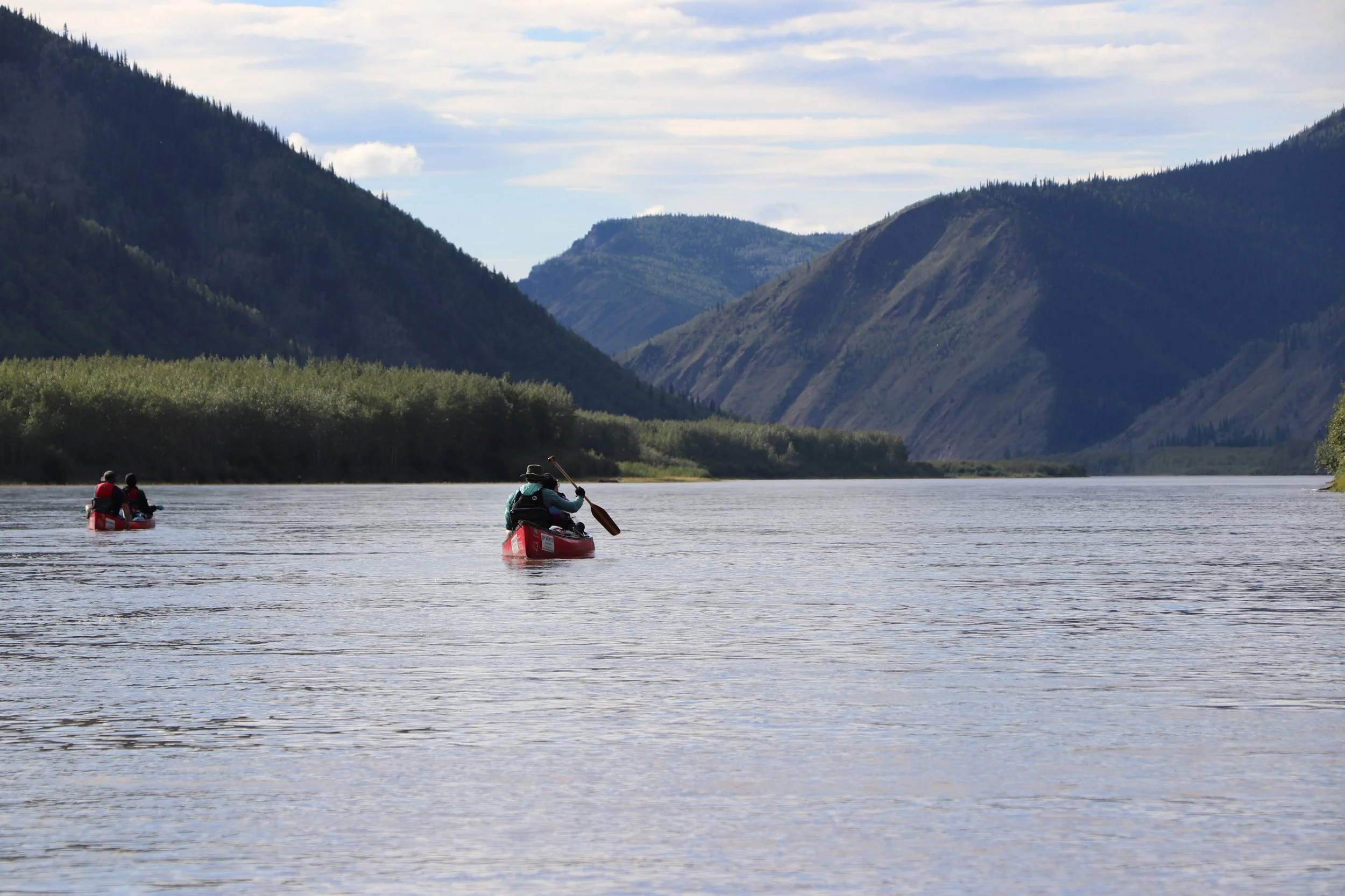 Canoeists paddling the Yukon River between forested hills.