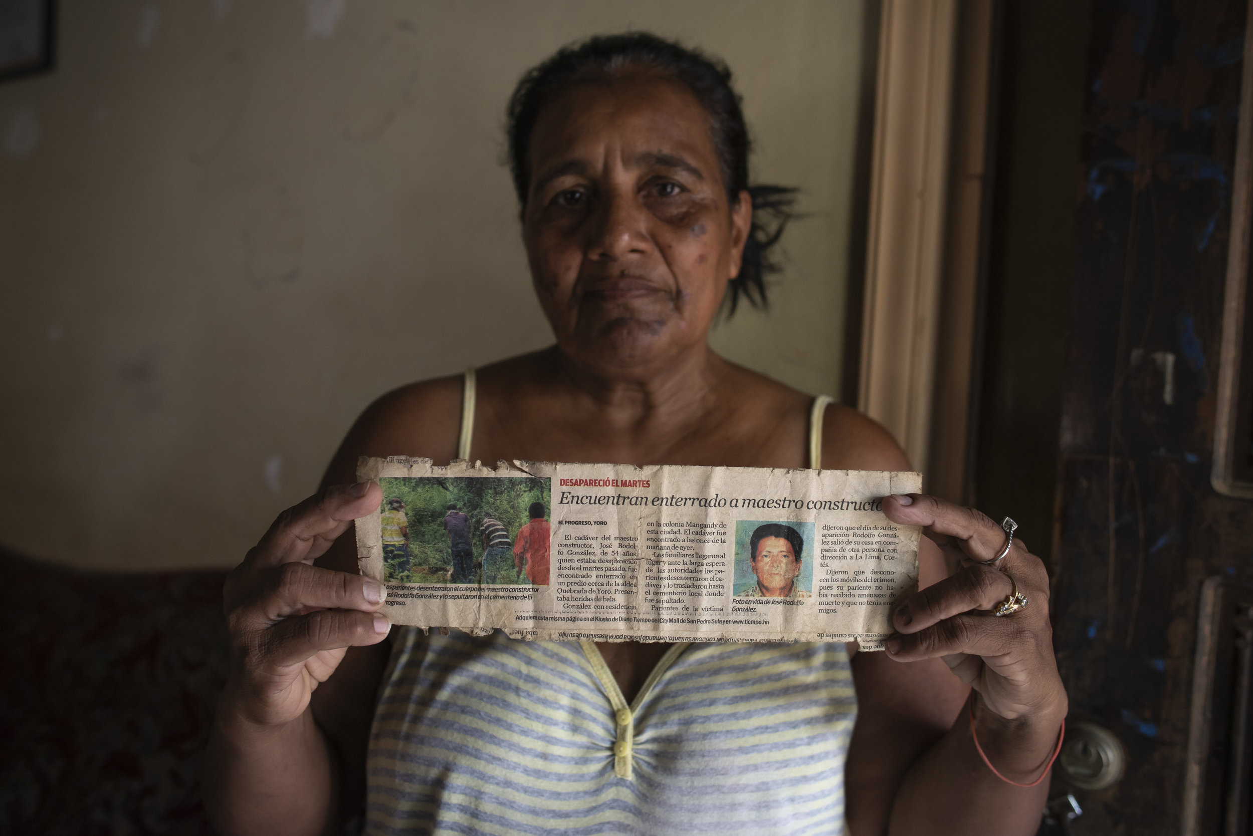  Delma Suyapa Hernandez holds up an article reporting on the murder of her husband. Since then, four of her sons have also been killed by gangs. El Progreso, Honduras. 