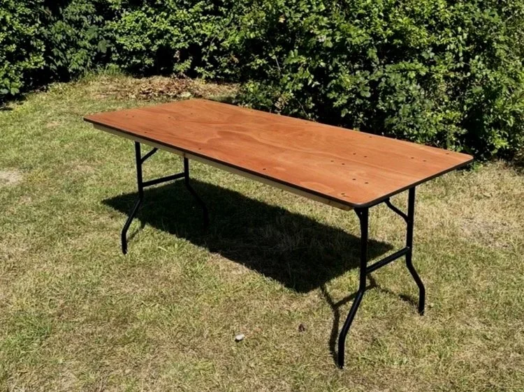 6ft ply top wooden trestle table with folding legs on grass available to hire.