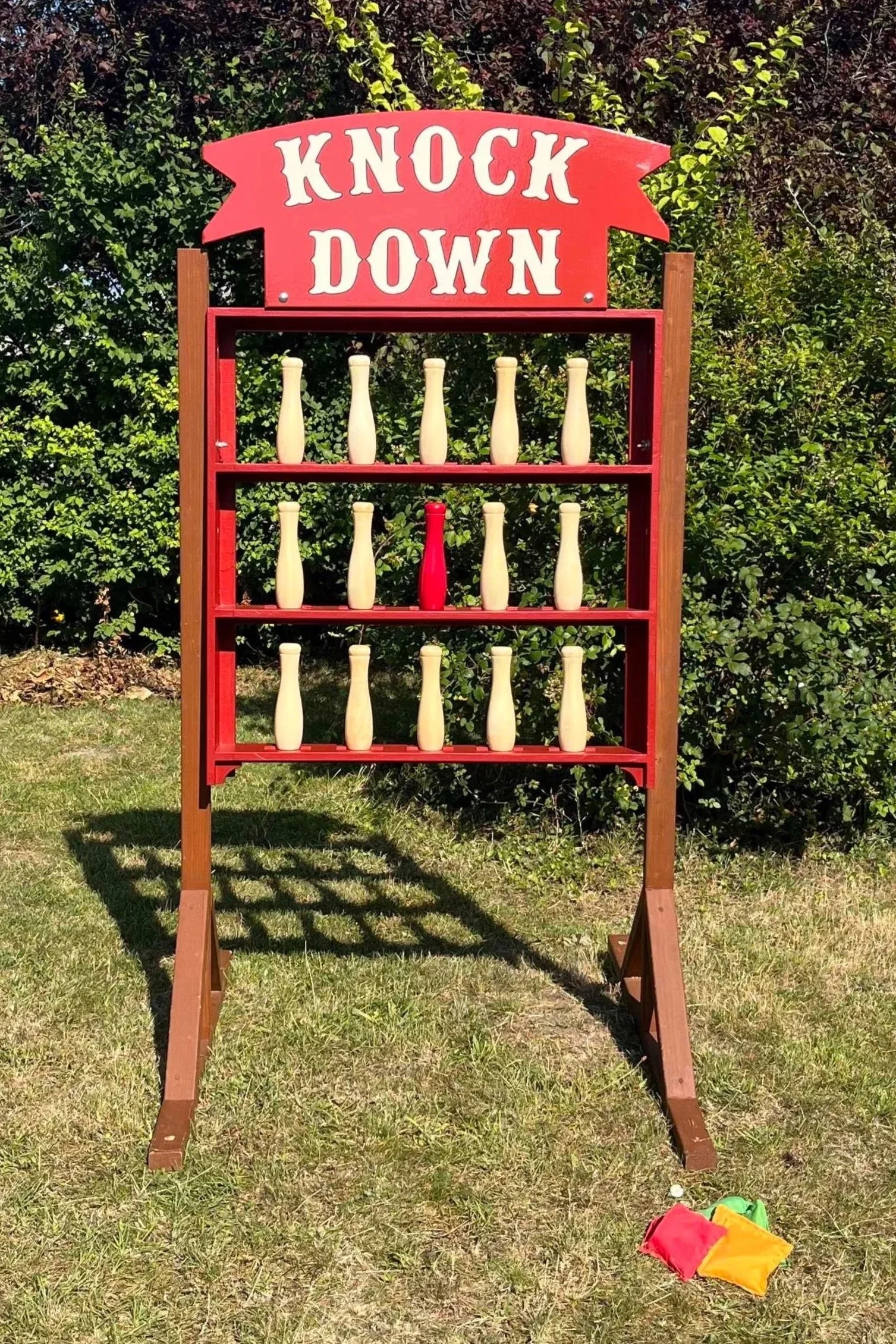 Knock Down Game, wood and red pins on a freestanding shelf with bold red and white sign and bean bags.