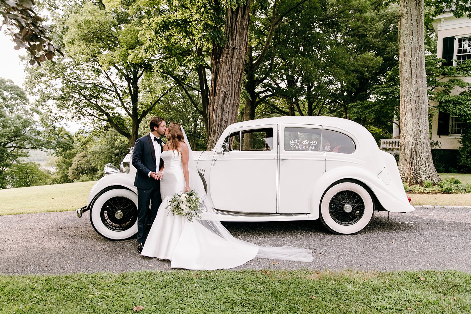 bride holding bouquet and groom in front of vintage getaway car