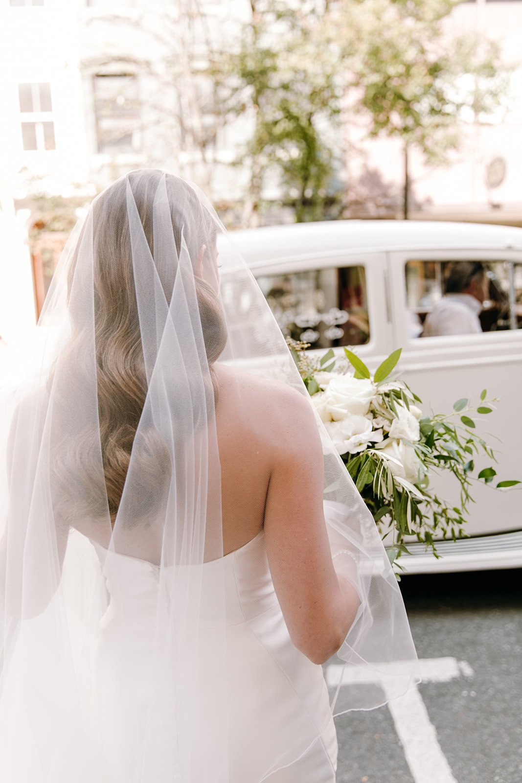 bride with veil walking to vintage car