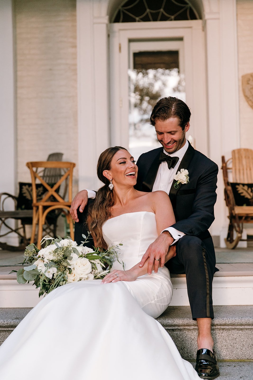 bride and groom giggling together on front steps with bridal bouquet in hand