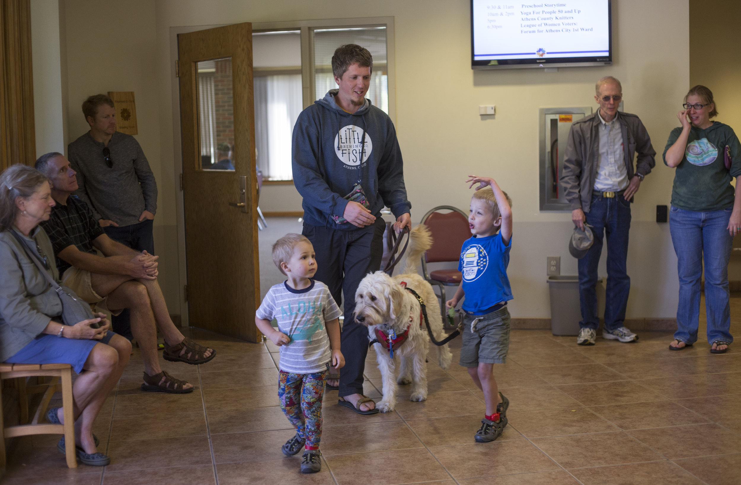  Josiah walks through the lobby of the Athens Public Library with Spad, his dad Jason, and his brother Judah while his mom Rachel, his grandfather Bruce Metzger, and others stand on the perimeter of the lobby. The library is now one of Josiah's favor