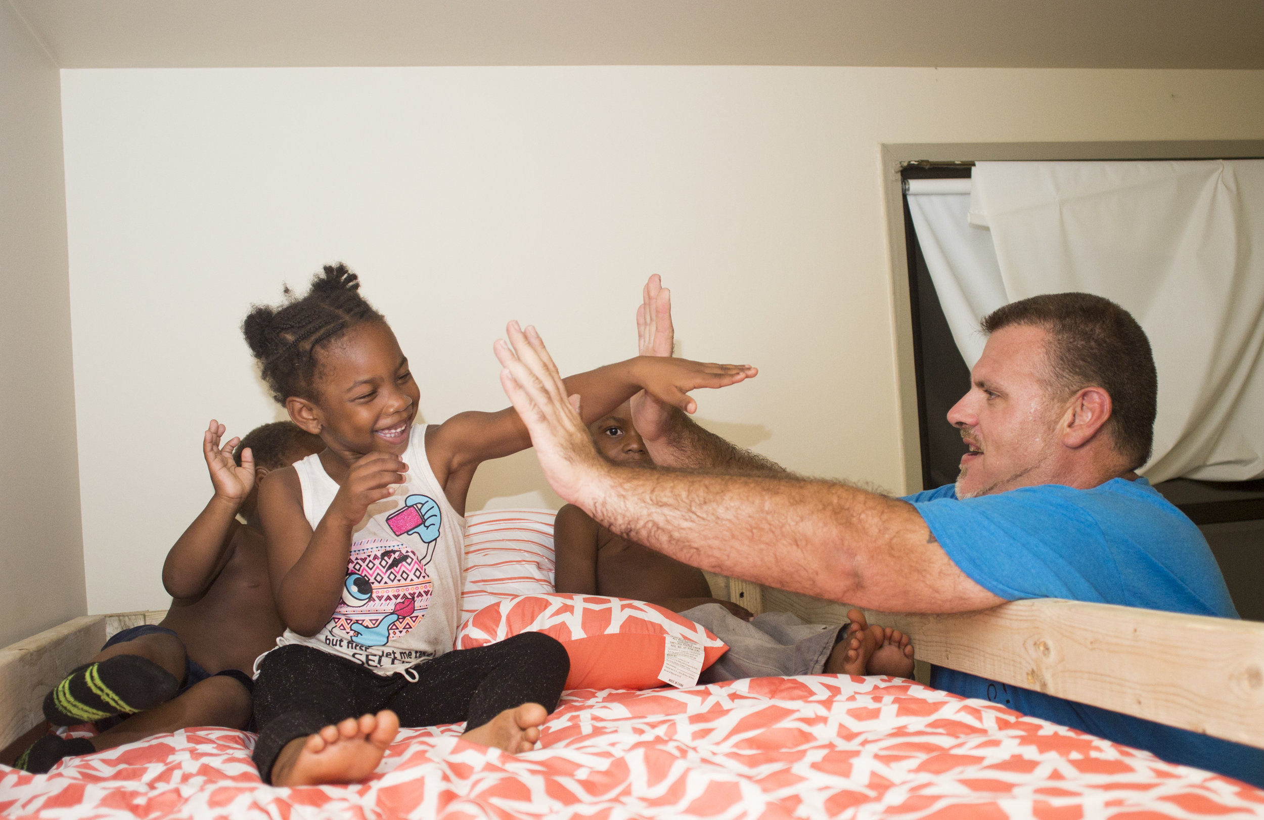  Dane "Mickey" Carder, of Canfield, Ohio, high-fives, from left, Xyayion Dotson, 3, Miracle Morgan, 5, and Zion Johnson, 4, while they sit in the top bunk of their new bunk bed from Sleep in Heavenly Peace in the kids' home in Campbell, Ohio, on the 