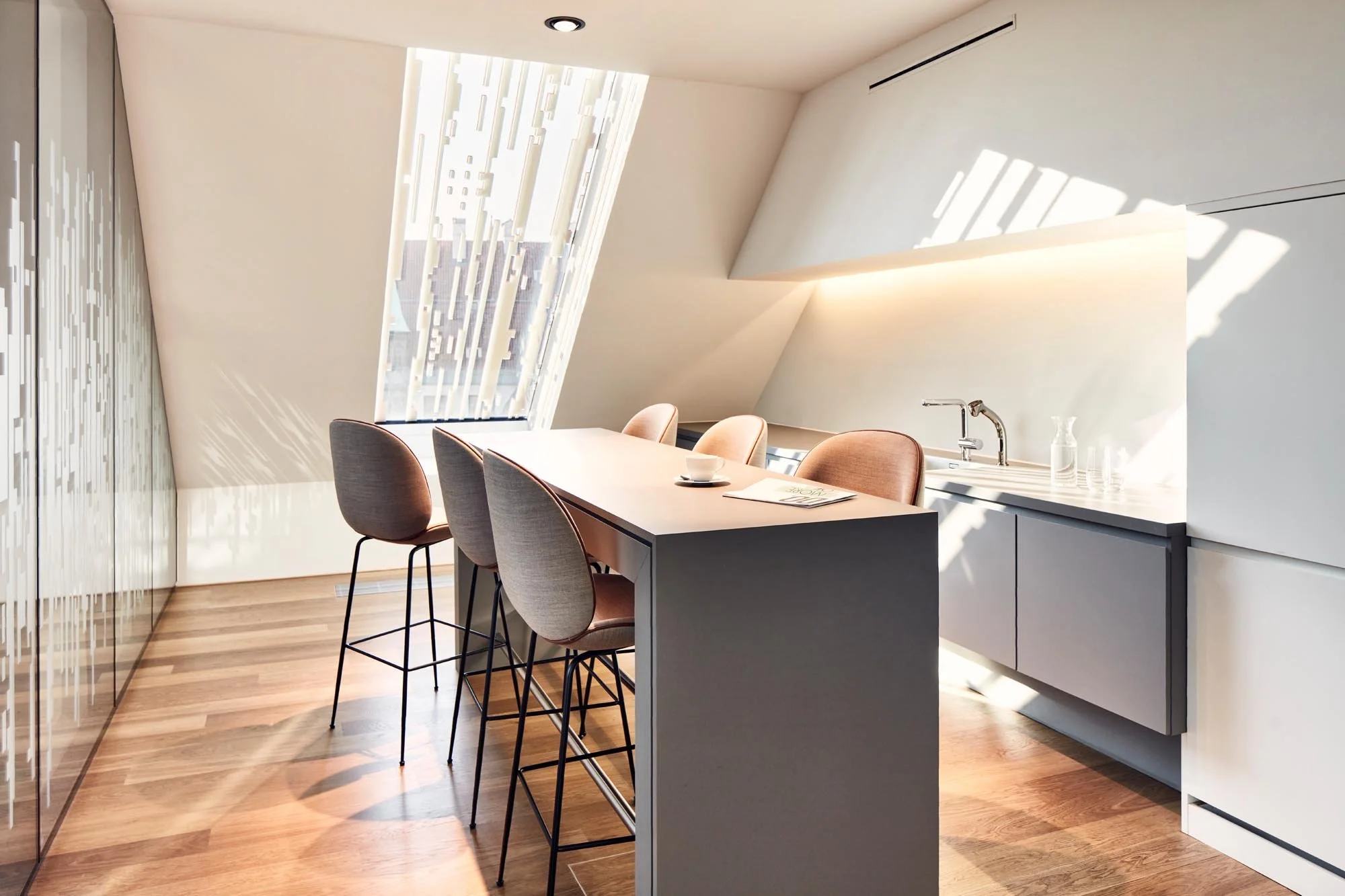 Helles, modernes Küchen- und Esszimmer mit einem hohen Esstisch und sechs Stühlen, unter Schrägdach mit großen Fenster, das natürliches Licht hineinlässt.