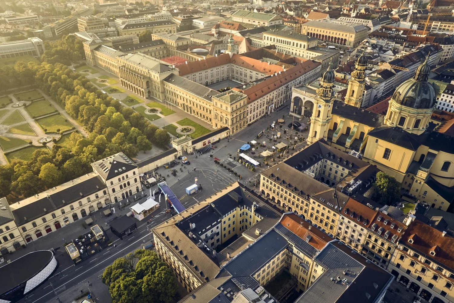 Luftaufnahme eines historischen Stadtzentrums mit barocker Kirche und einem großen Park auf der linken Seite, außerdem Marktstände im öffentlichen Platz