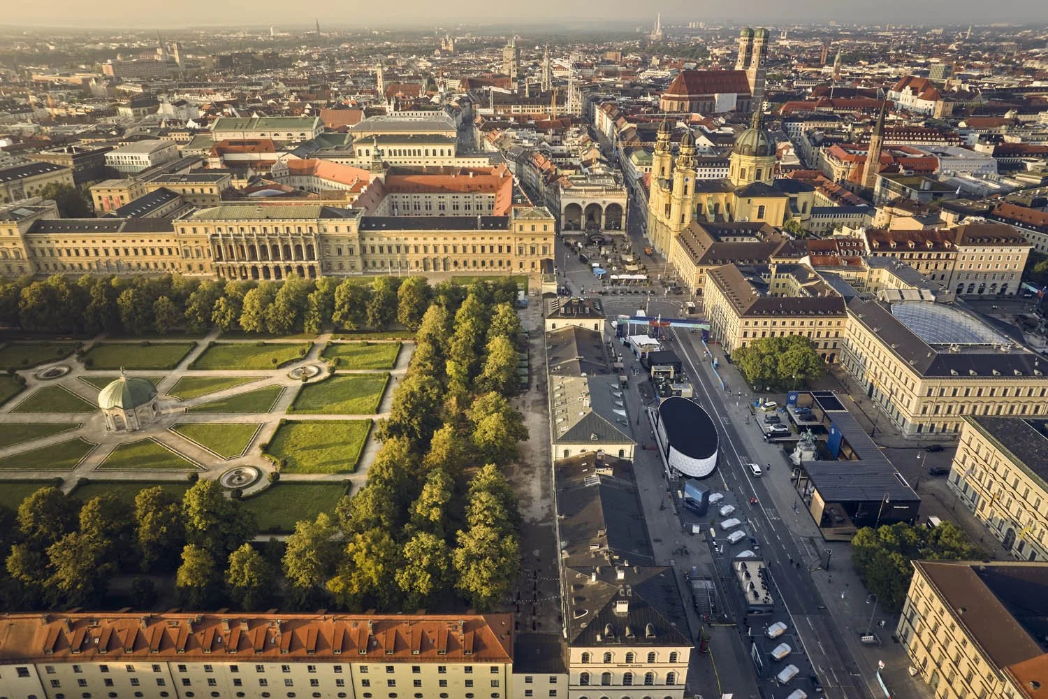 Luftaufnahme einer europäischen Stadt mit historischem Stadttor, Kirchen, grünen Parks und Straßen mit Autos, bei Sonnenuntergang.