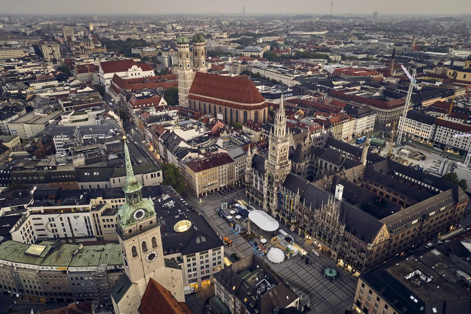 Luftaufnahme eines historischen Stadtplatzes in München, Deutschland, mit gotischer Kirche, Rathaus mit Uhrturm, umliegenden multidimensionalen Gebäuden und Baustellen im Hintergrund.