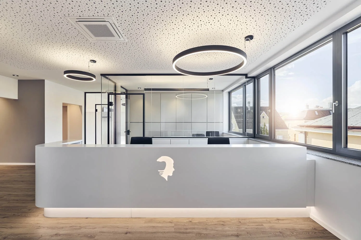 Modernes Büro mit weißen Wänden, großem Fenster, Holzfußboden und eleganten runden Deckenleuchten.