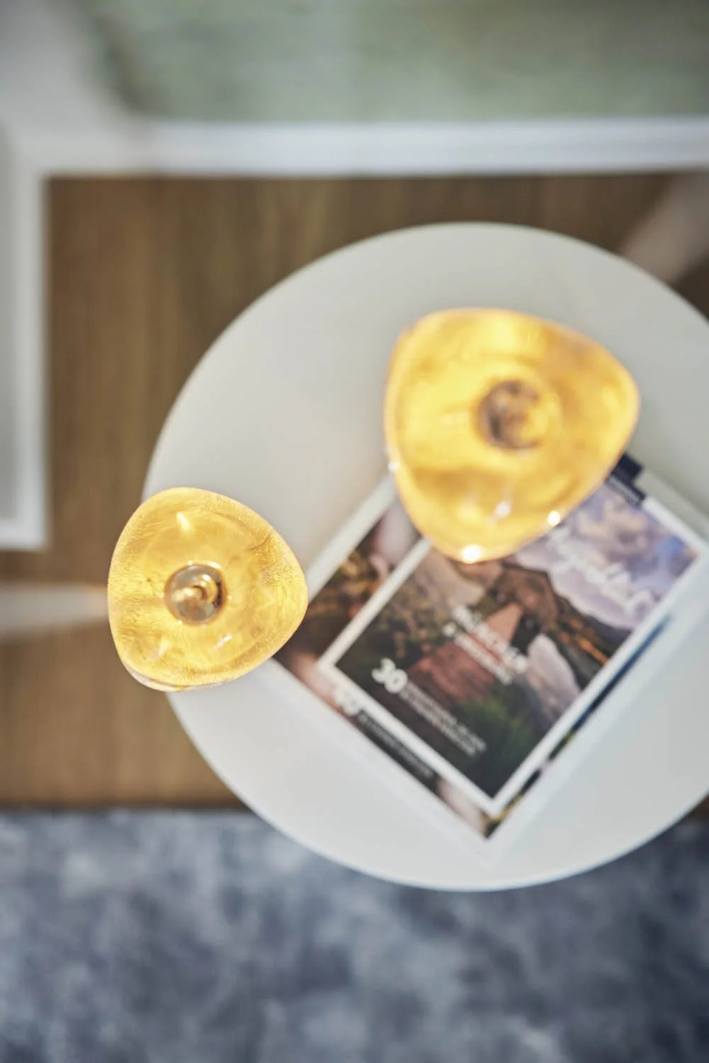 Zwei goldene Tischlampen auf einem weißen runden Tisch mit einer Broschüre. Innenarchitektur Villa Grünwald Raum und Licht