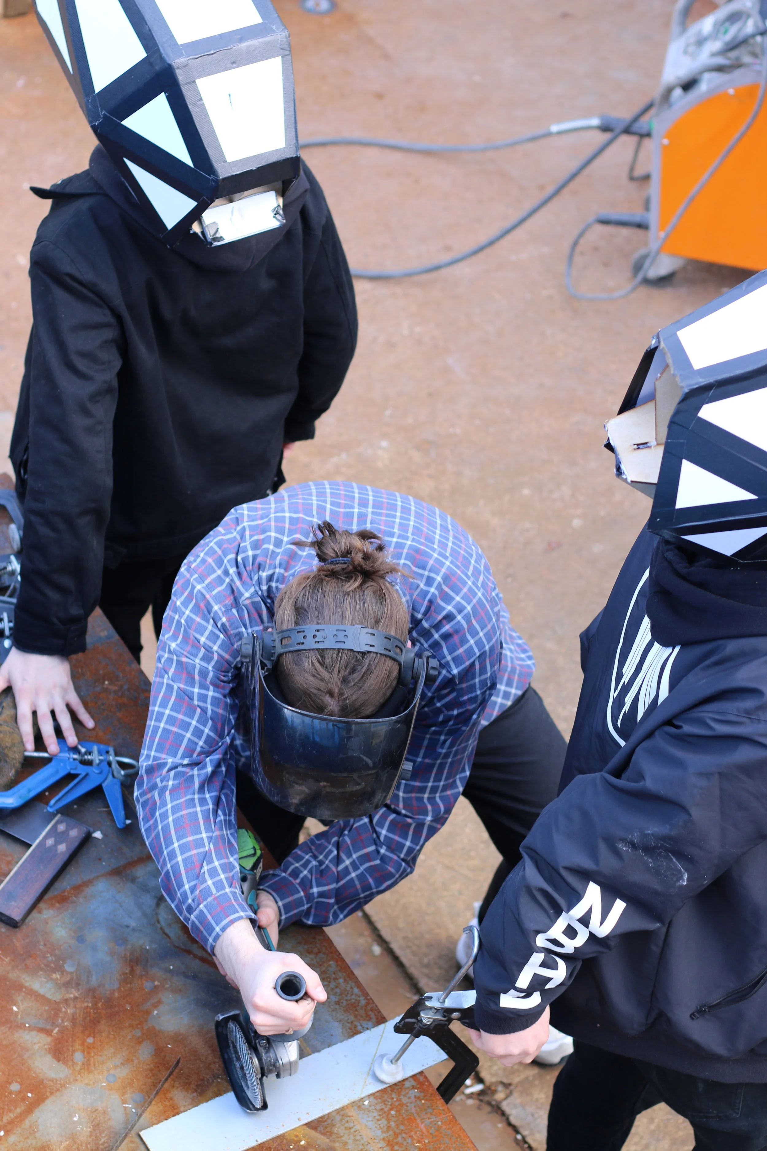 Reversants assisting a human who is angle grinding at a workshop.