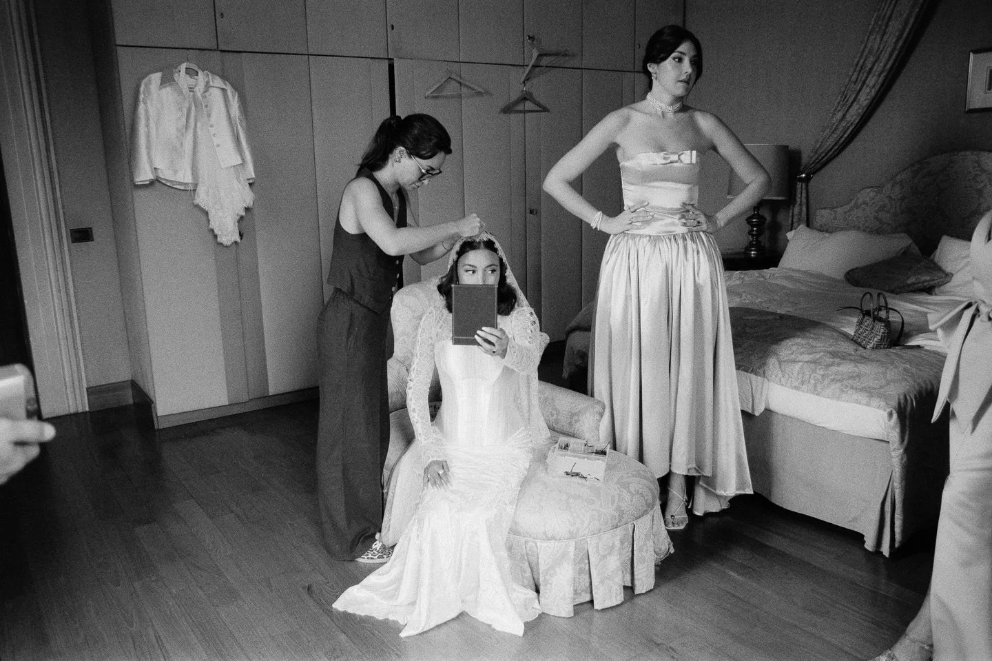 I’m captivated by this moment. While Giulia is placing Saige’s veil, her second dress hangs patiently, waiting for the night to come; the other hangers seem to be caught in a little dance.
Someone says something off frame, and the gazes