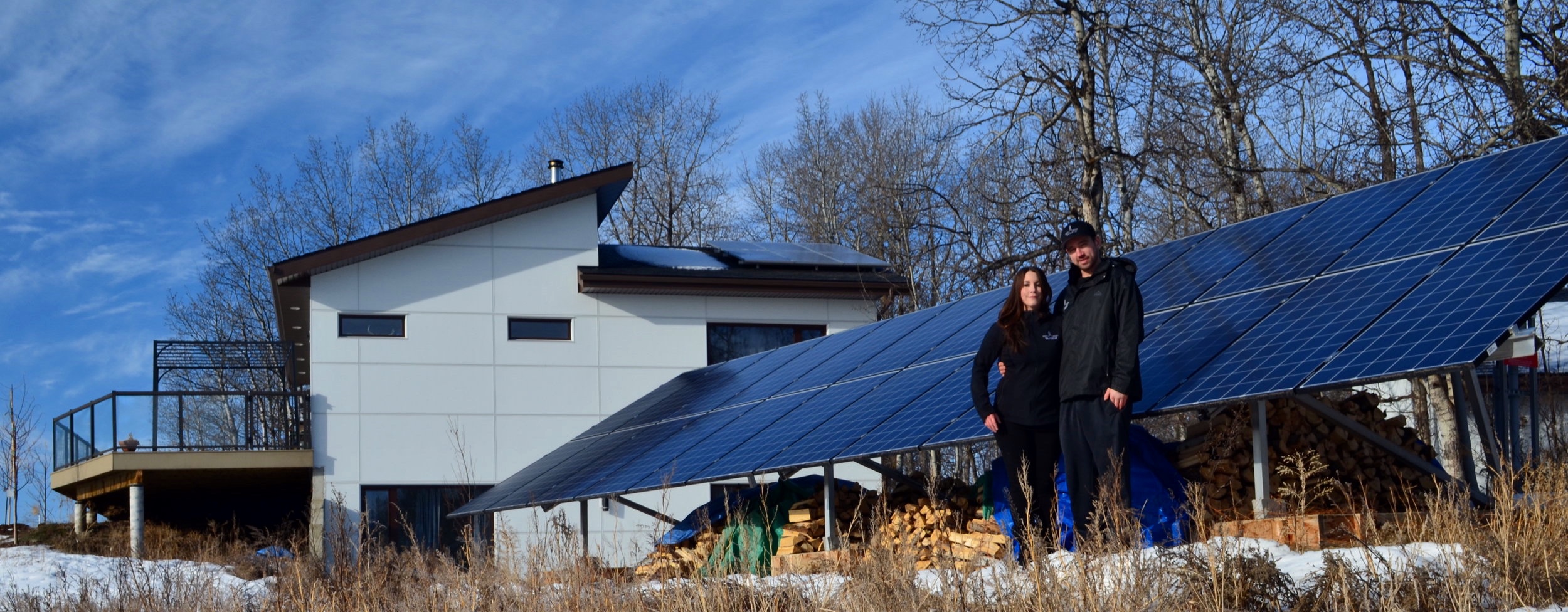 Standing in front of the ground-mount “off-grid” portion of our solar system. You can see the wood stored underneath, as the panels provide a dual purpose!