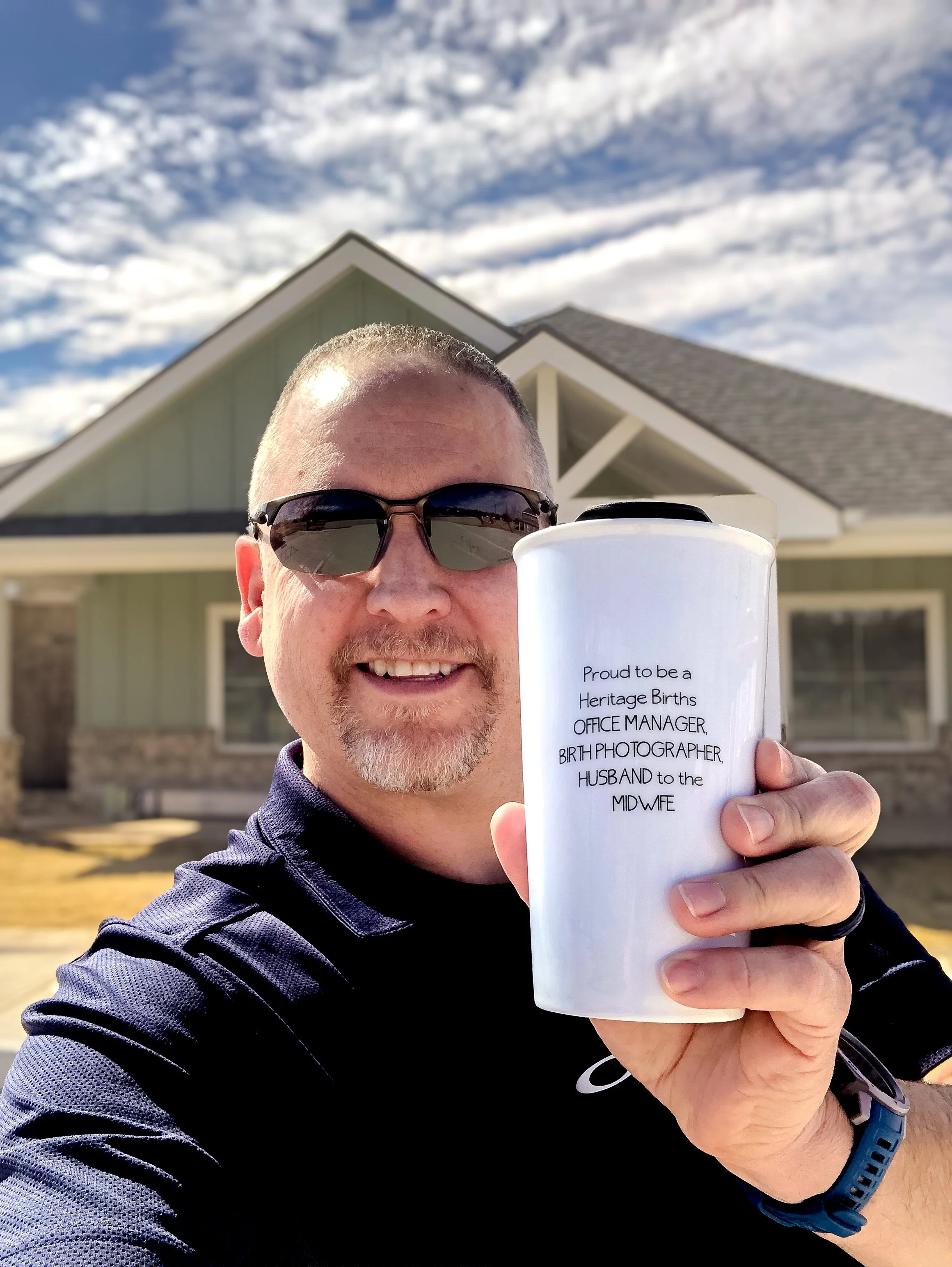 Jeff holding a tumbler that reads: Proud to be office manager, birth photographer and Husband to the Midwife.