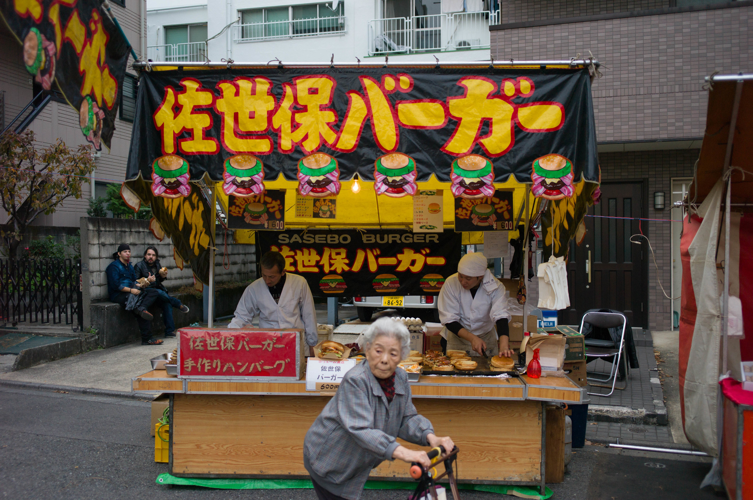 Elderly woman passes a hamburger stand at the Gishi-sai festival in Tokyo, December 14, 2015.