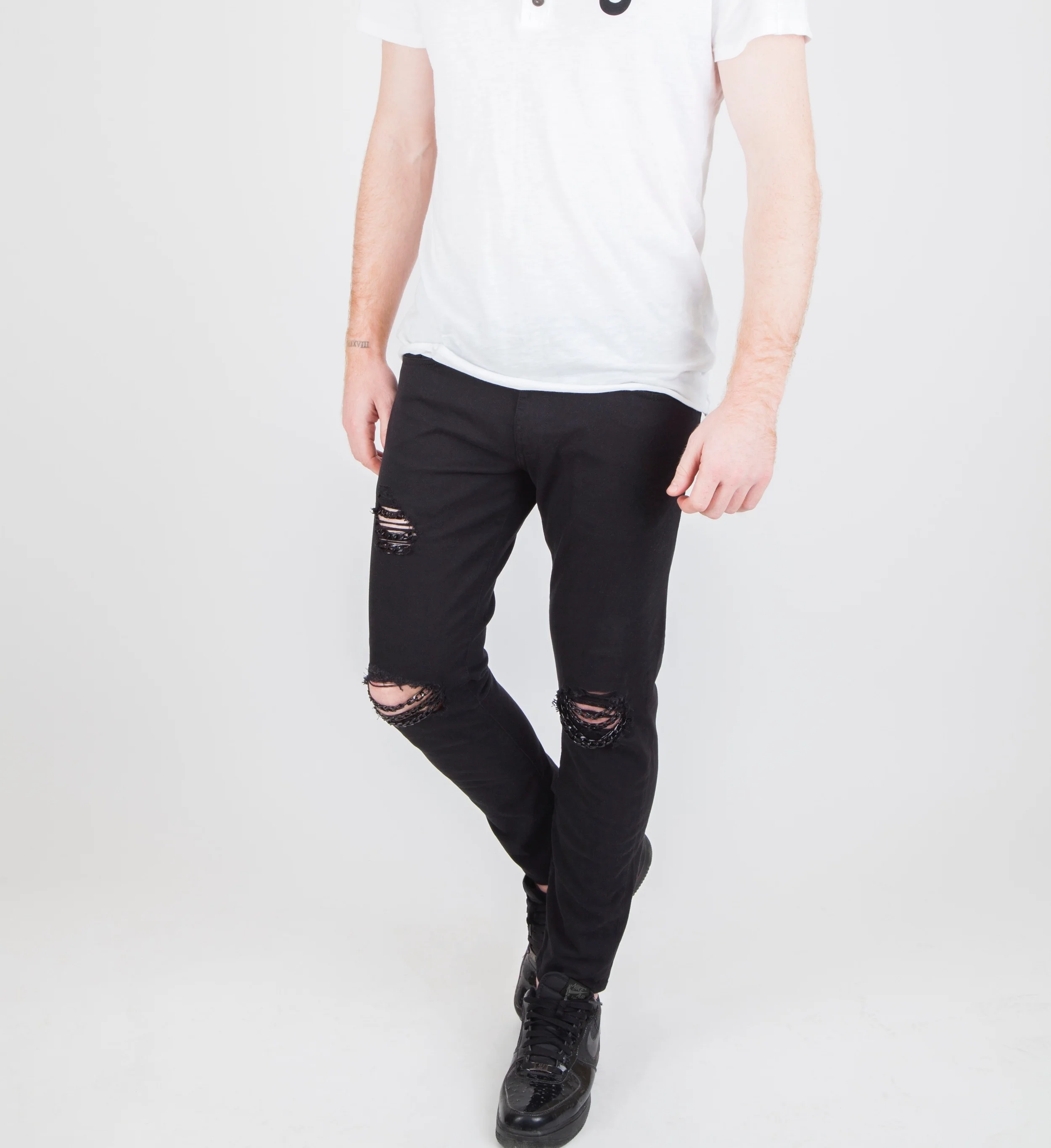 Mens black skinny jeans distressed with the holes at the knee and thigh with black chains and a white tee shirt
