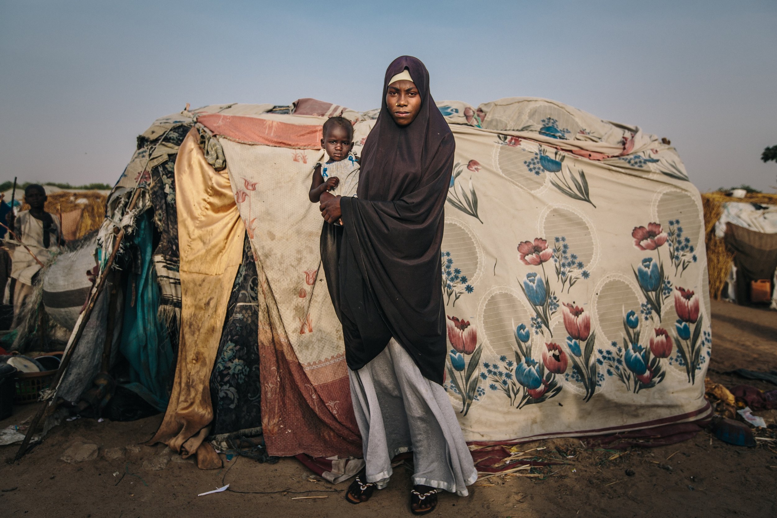 A woman and her child pose outside of their makeshift home built from a collection of fabrics inside the Farm Centre IDPs camp in Maiduguri, Nigeria