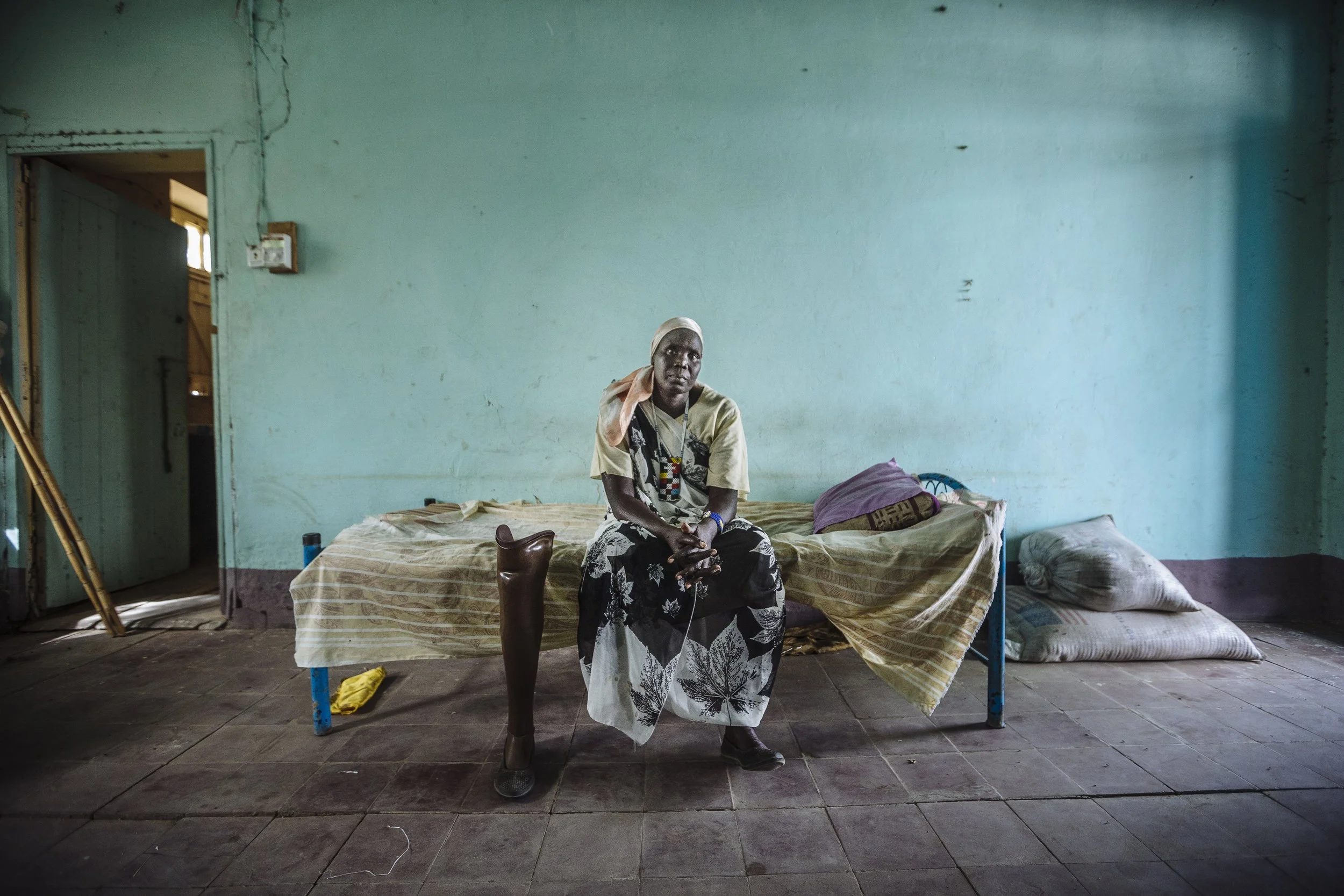 Sitting on a bed within a church compound, Sarah Nyan Gan Makuei is among the many former residents of the Malakal PoC. An opportunity came for Sarah and her family to escape to Juba through a chartered flight offered by a local oil company but she and her family had to travel to the remote town of Paloich to catch it. Sarah had lost her leg in 1995 in a car accident. Unable to make the long trek up to Paloich, she made the difficult decision to stay behind while her husband took their six children to Juba in hope of a better life.