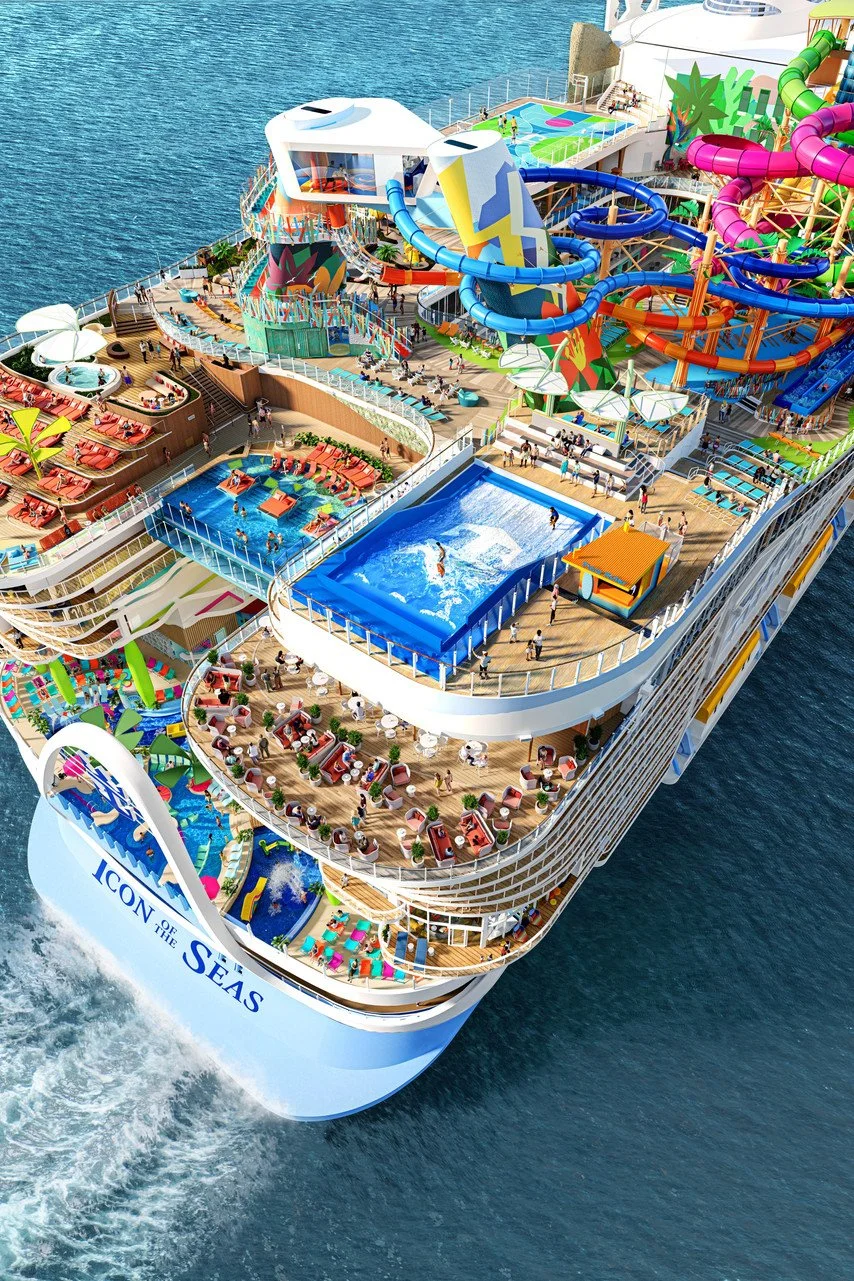 Aerial view of a cruise ship with multiple swimming pools, water slides, and recreational areas on the deck, sailing on the ocean.