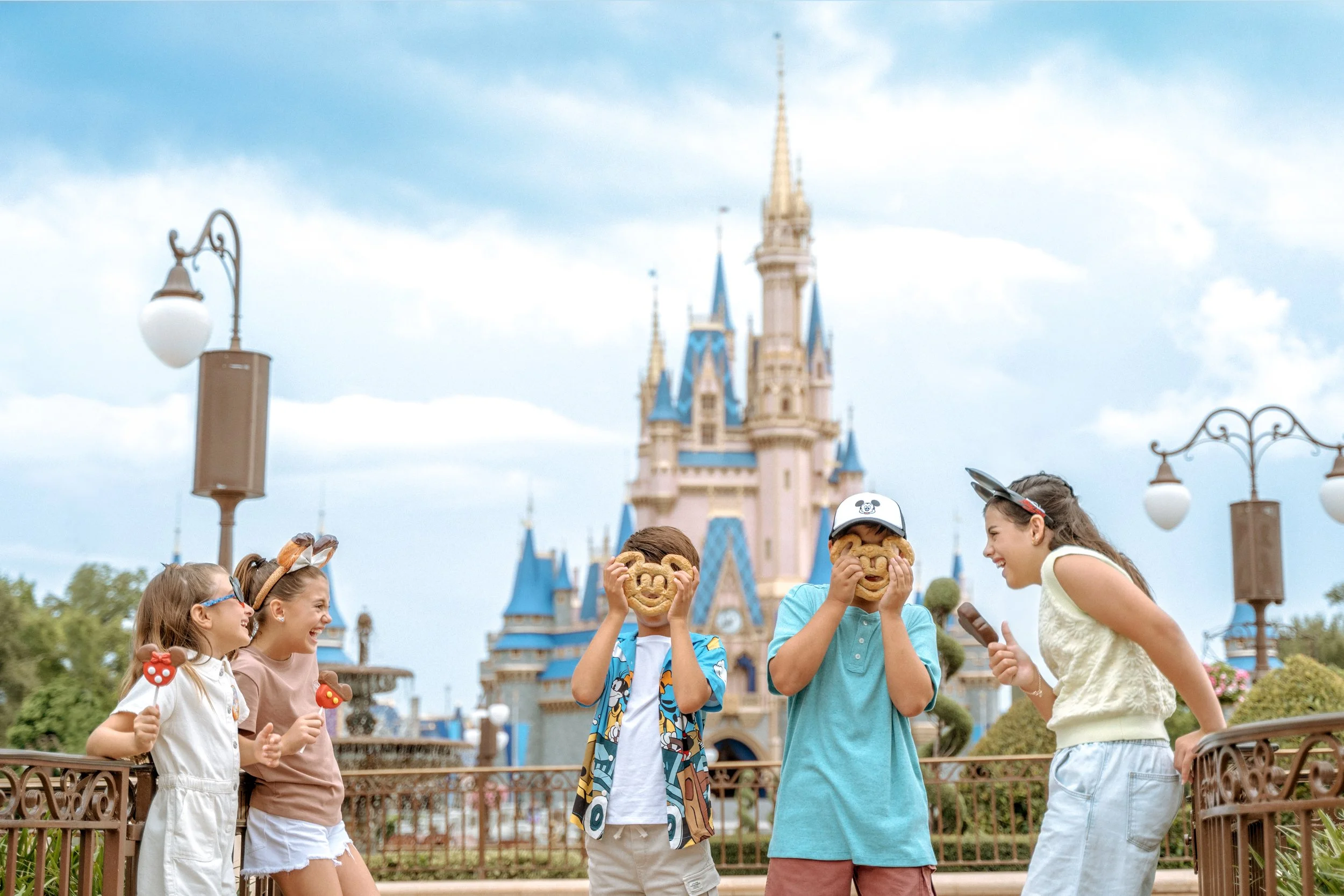 Two young girls dressed as Disney Snow White characters happily holding purple and white swirled lollipops in front of a castle at a theme park.