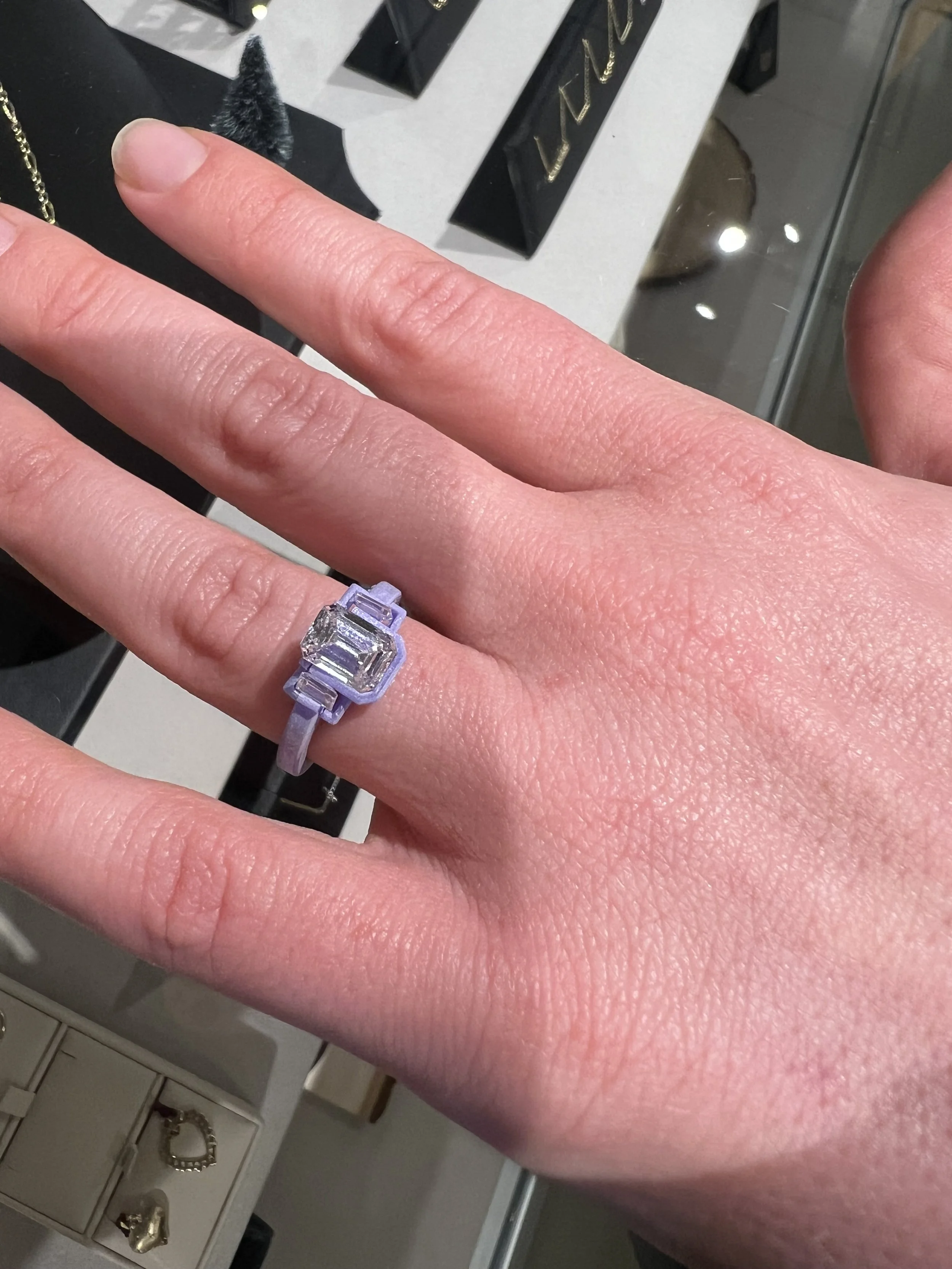 A person holding a small purple 3D-printed ring with intricate details resembling a dragon or military design.