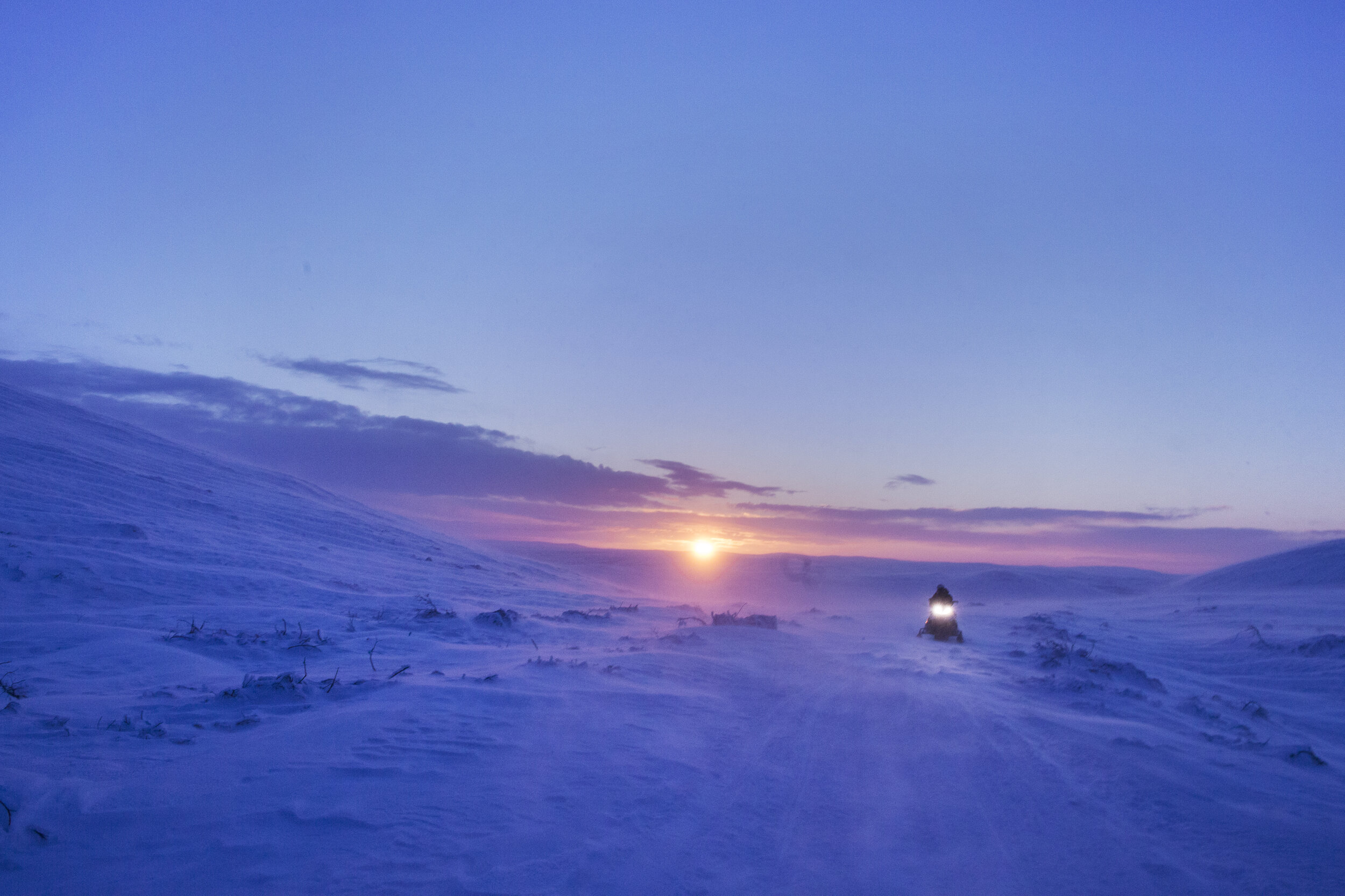  En reindriftsutøver kjører snøscooter innover vidda utenfor Kautokeino mens solen står opp bak ham. A reindeer herder is driving his snow scooter over the mountain plateau outside of Kautokeino, Norway, while the sun is rising behind him.  