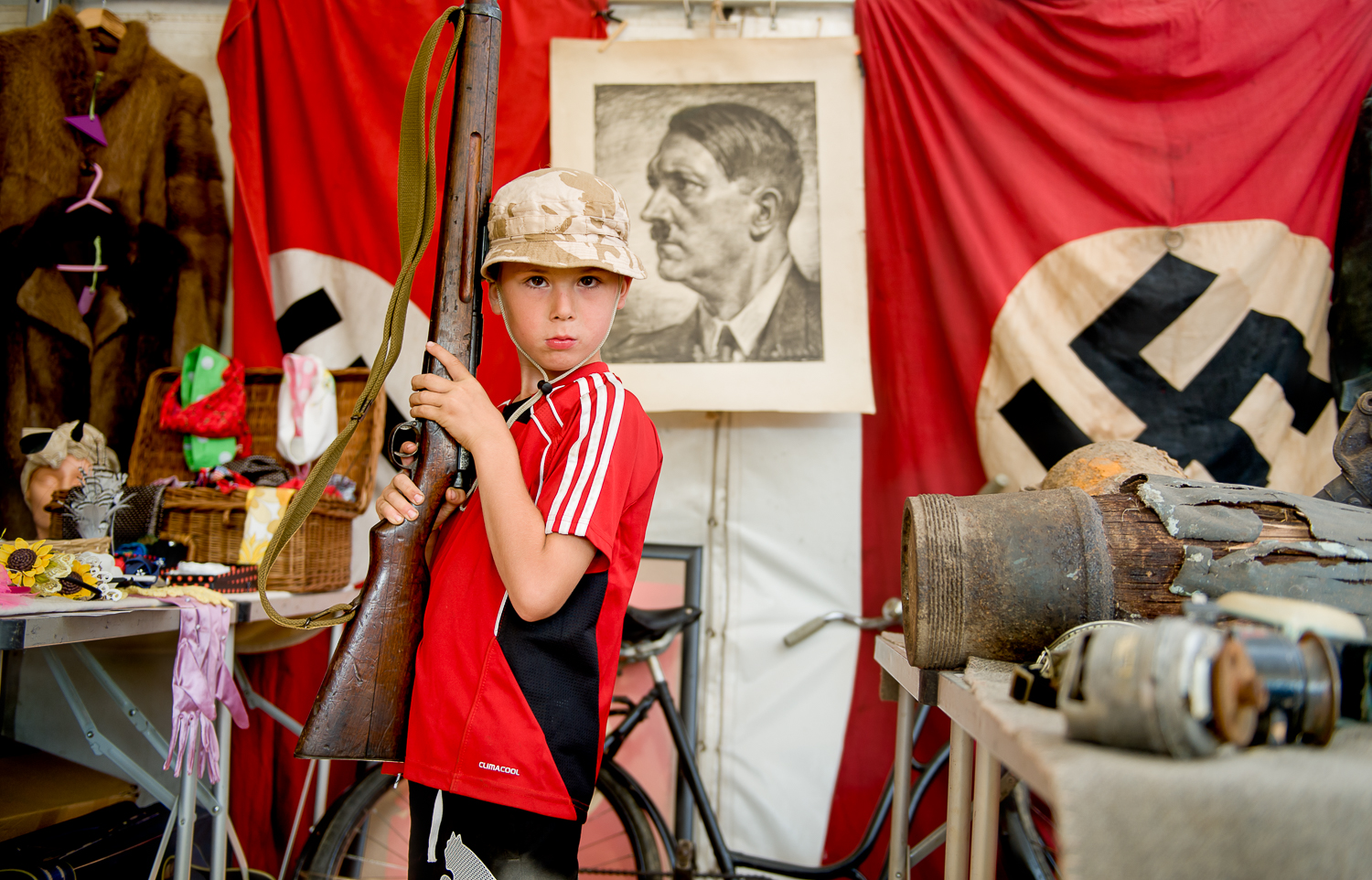  young visitor to War and Peach show posing with rifle, shot in a memorabilia tent selling original items from WW2. 