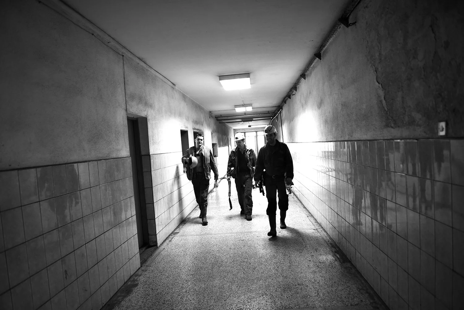 Coal miners walk down the hall, they gather in the main room before the shift begins.