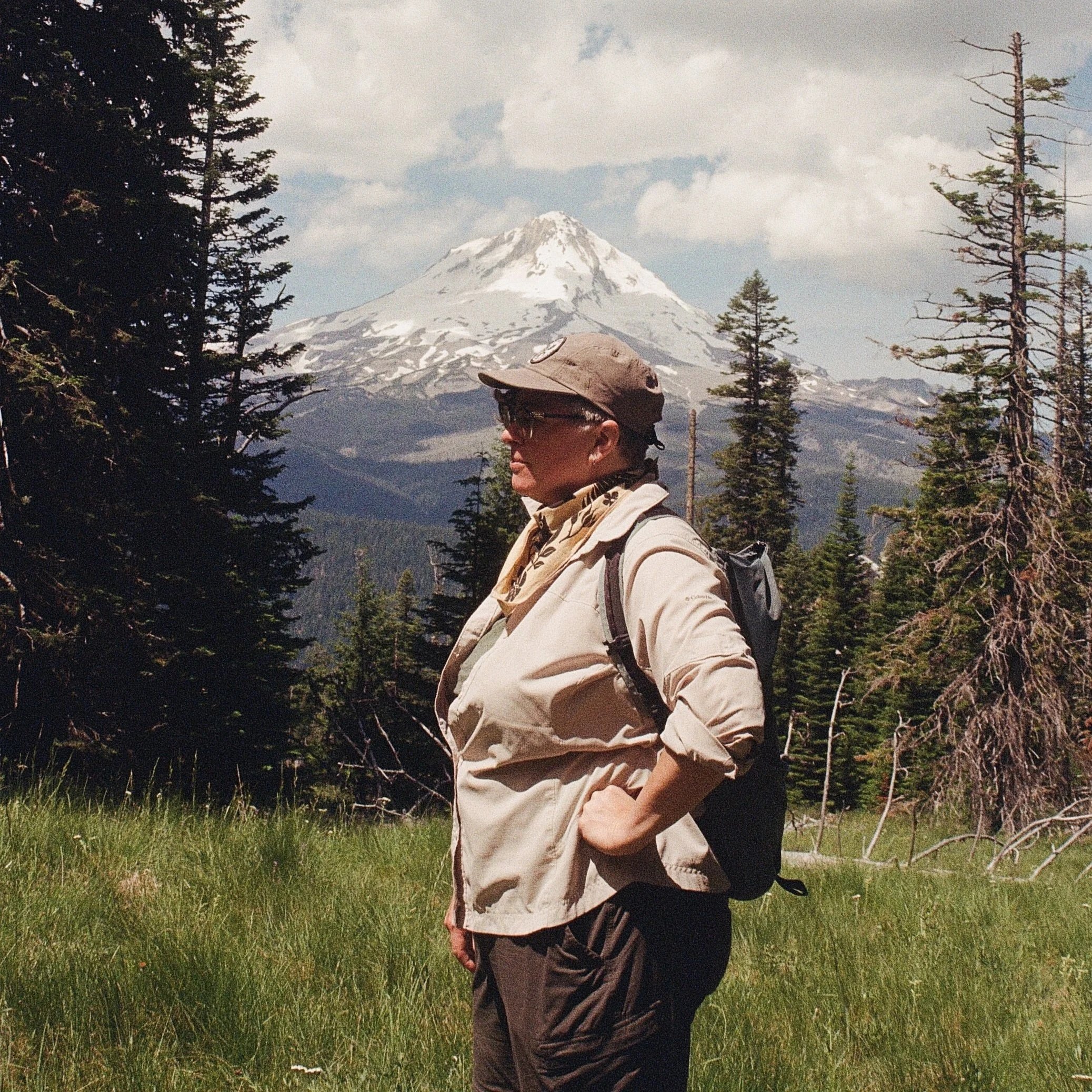 A person hiking outdoors with a mountain in the background and tall trees surrounding them.
