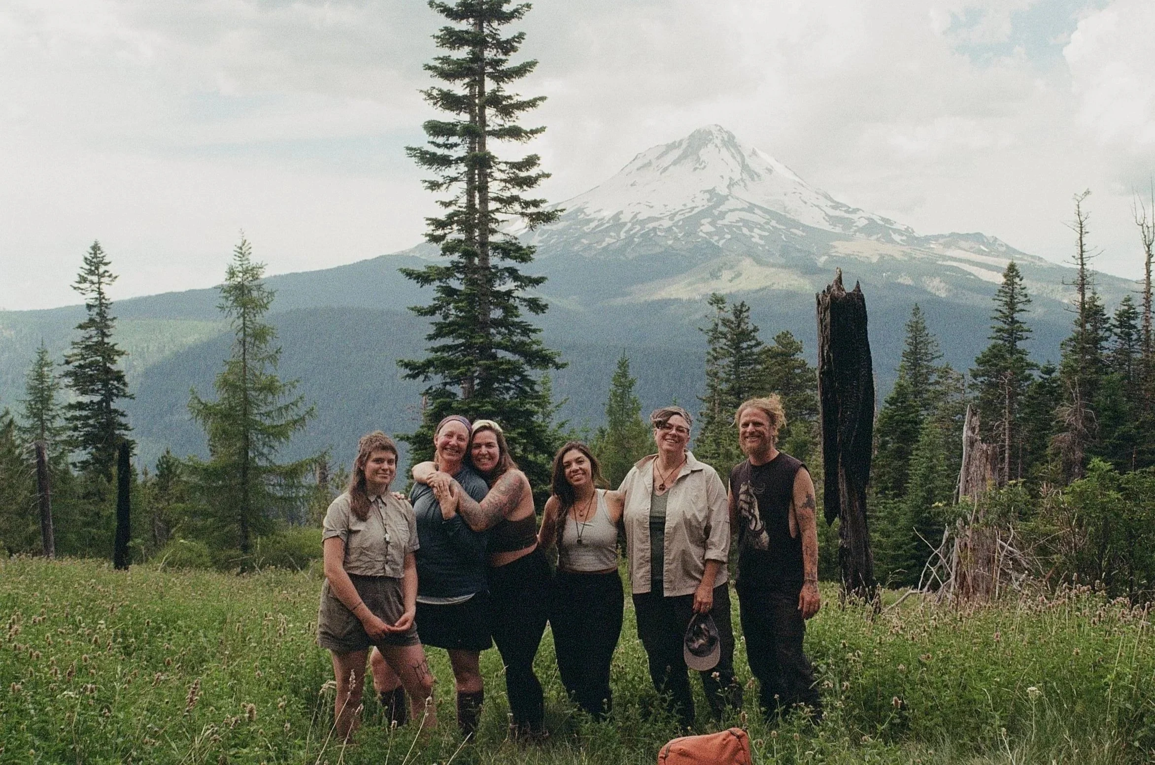 Group of seven people standing outdoors in a forested area with Mount St. Helens in the background.