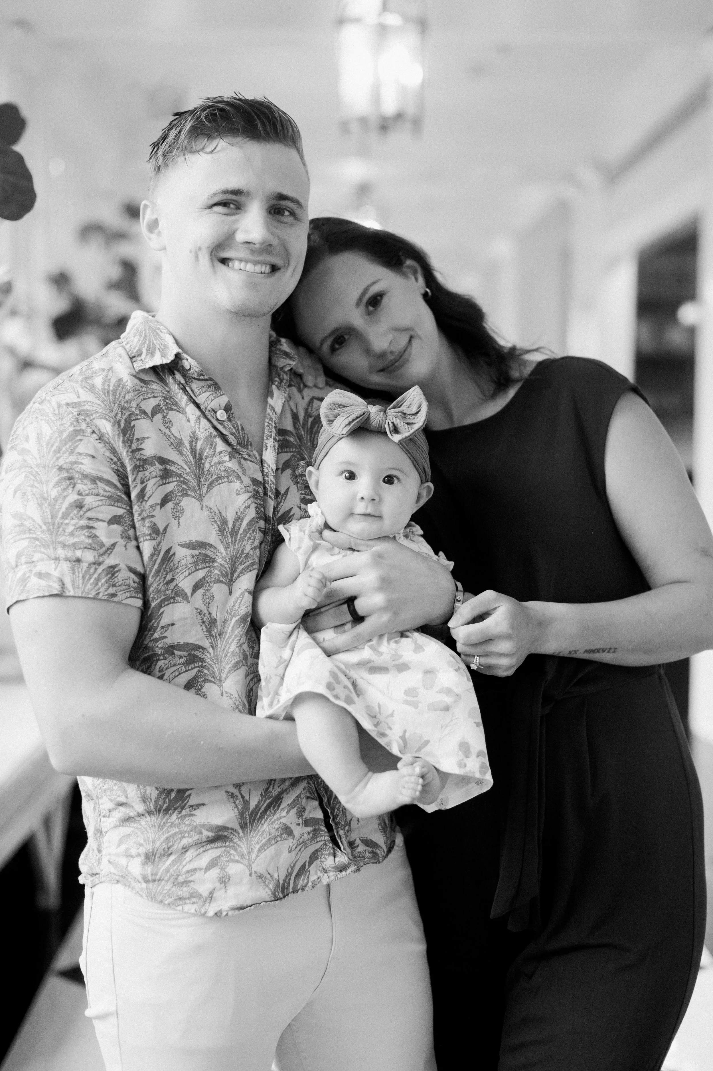 A smiling man and woman holding a baby girl in an indoor setting.