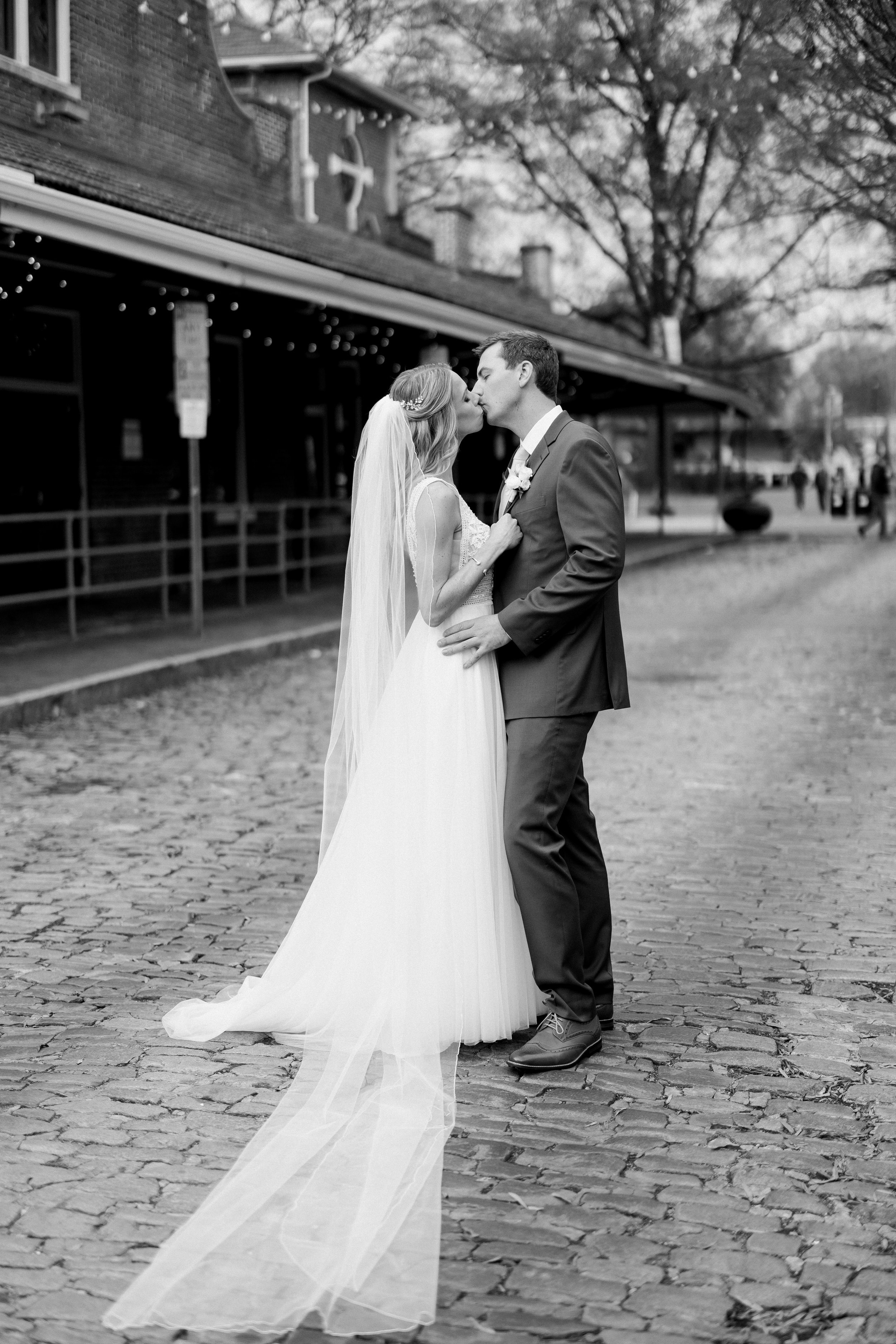Bride and groom kissing on the cobblestone street outside Market Hall in Raleigh