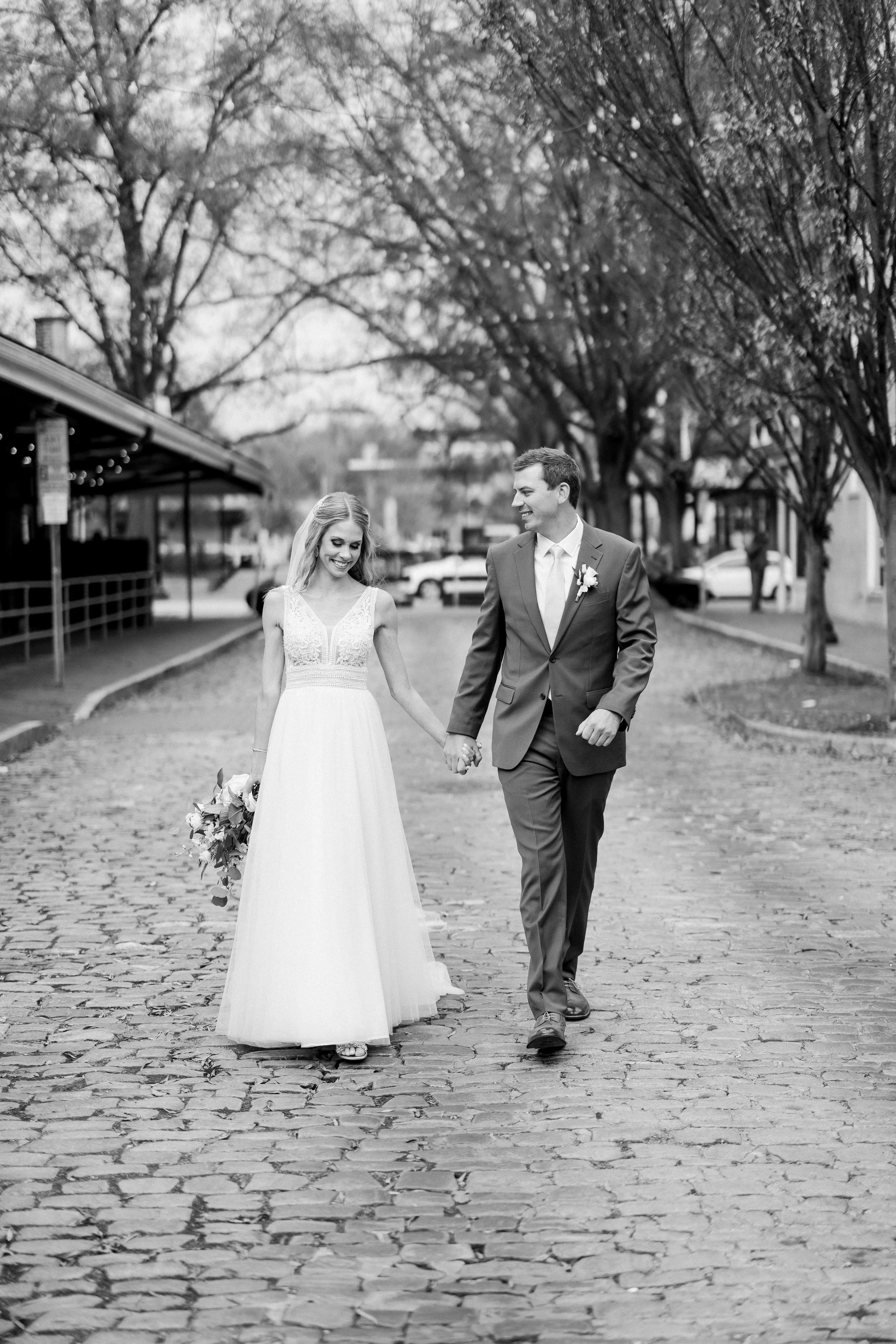 Bride and groom holding hands and walking down the cobblestone street at Market Hall in Raleigh