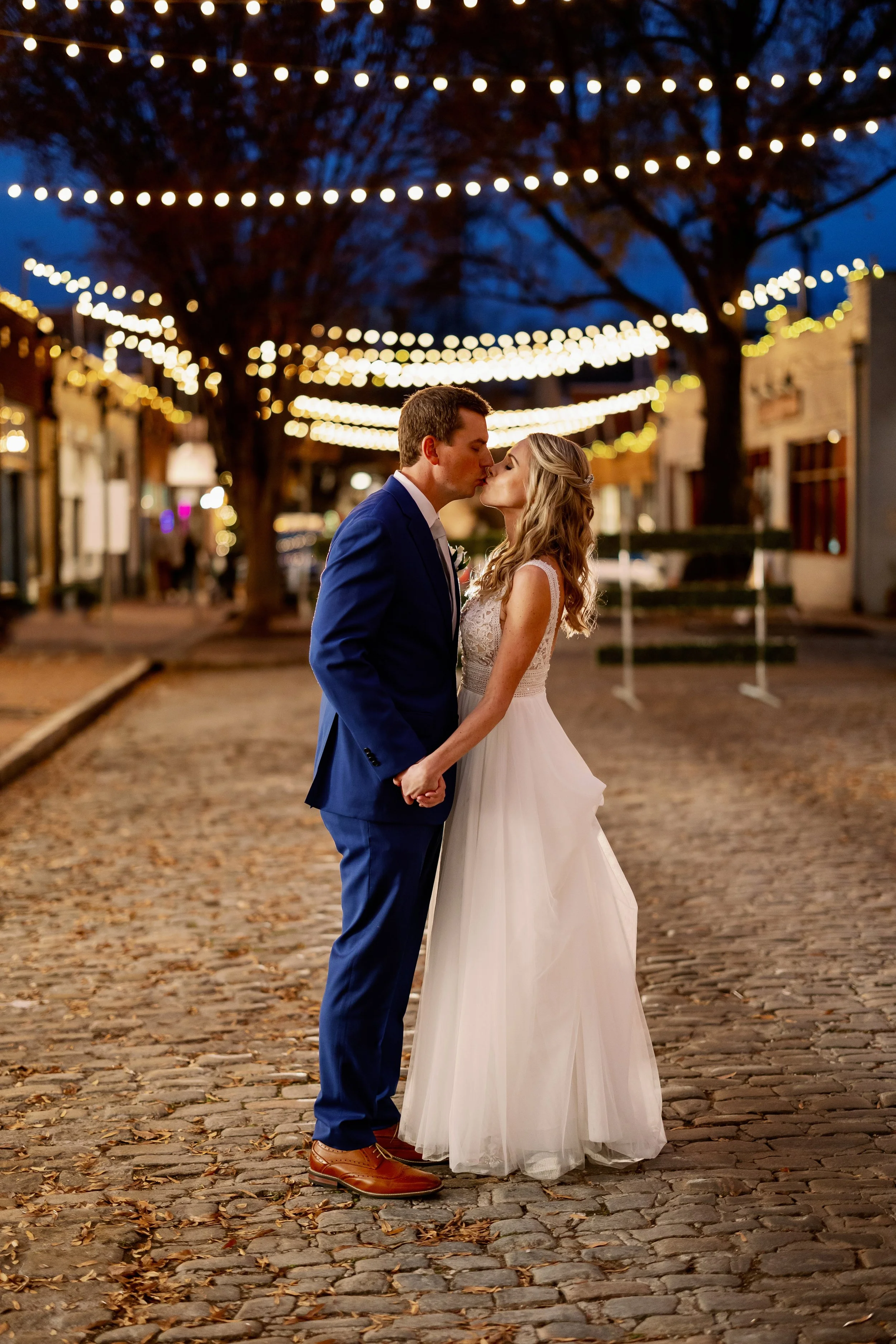 Bride and groom kissing under Market Hall string lights during their Raleigh wedding
