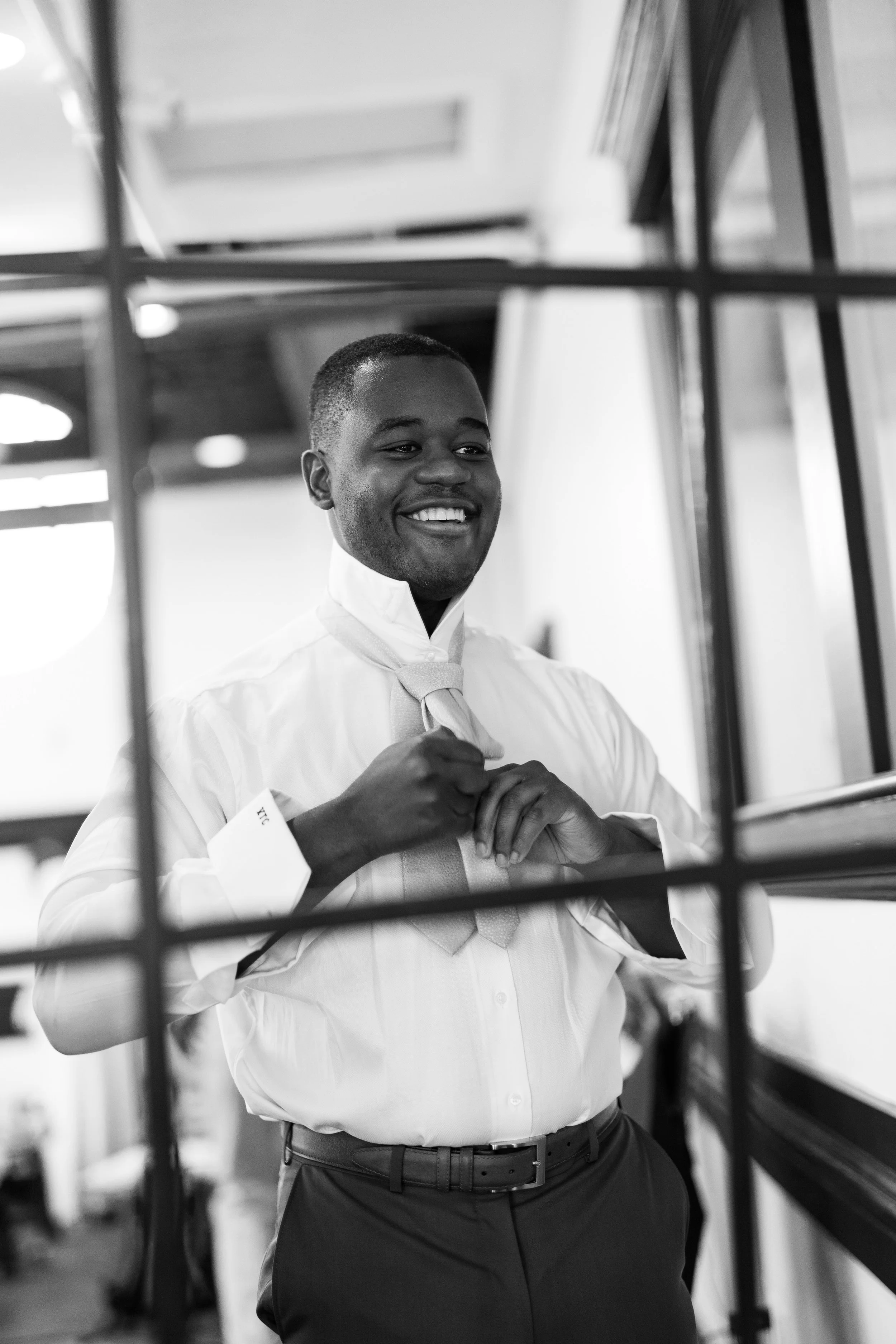 Groom smiling while adjusting his tie before the wedding at Market Hall in Raleigh NC