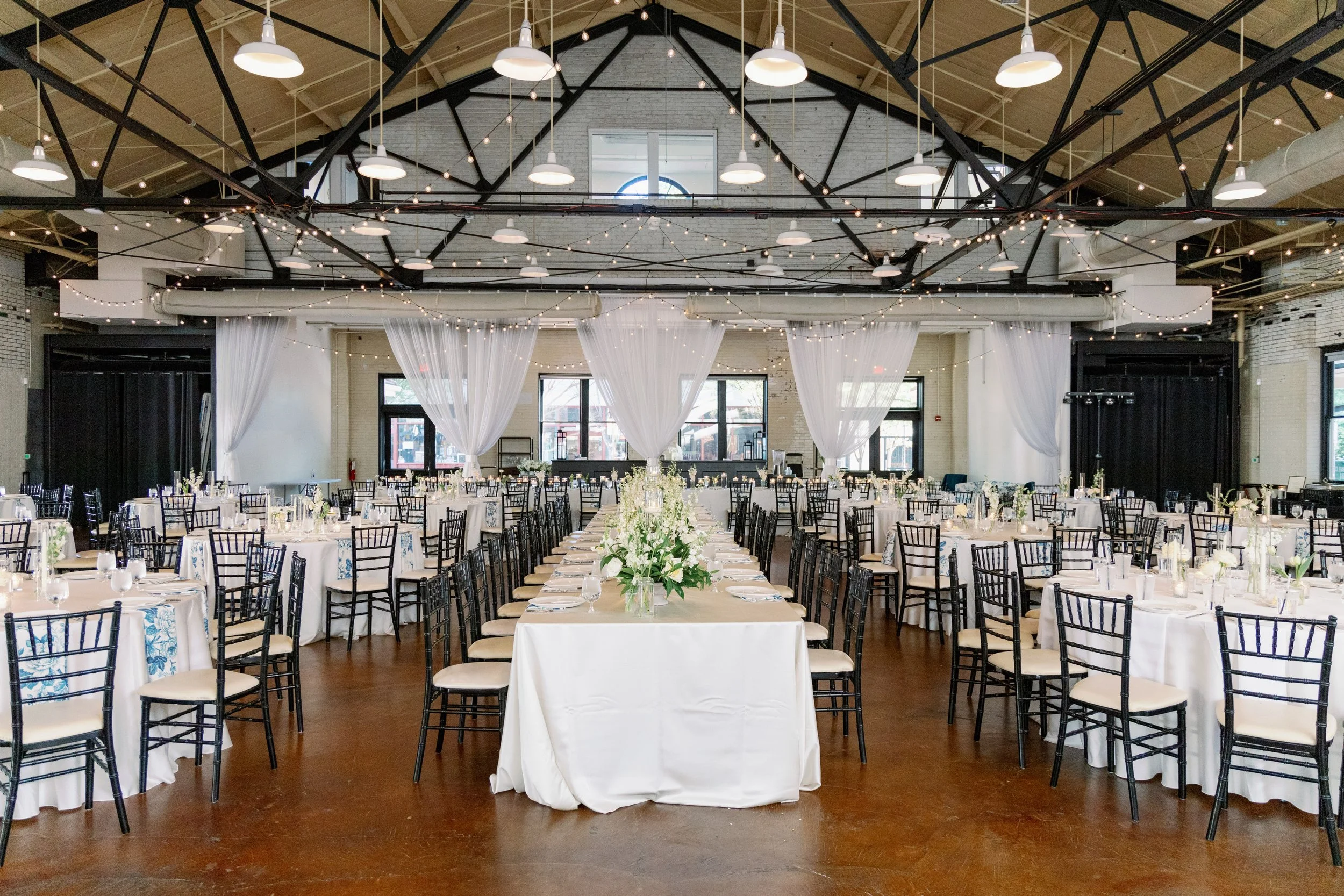 Market Hall reception layout with long tables, white linens, black chairs, and draped fabric in Raleigh NC 