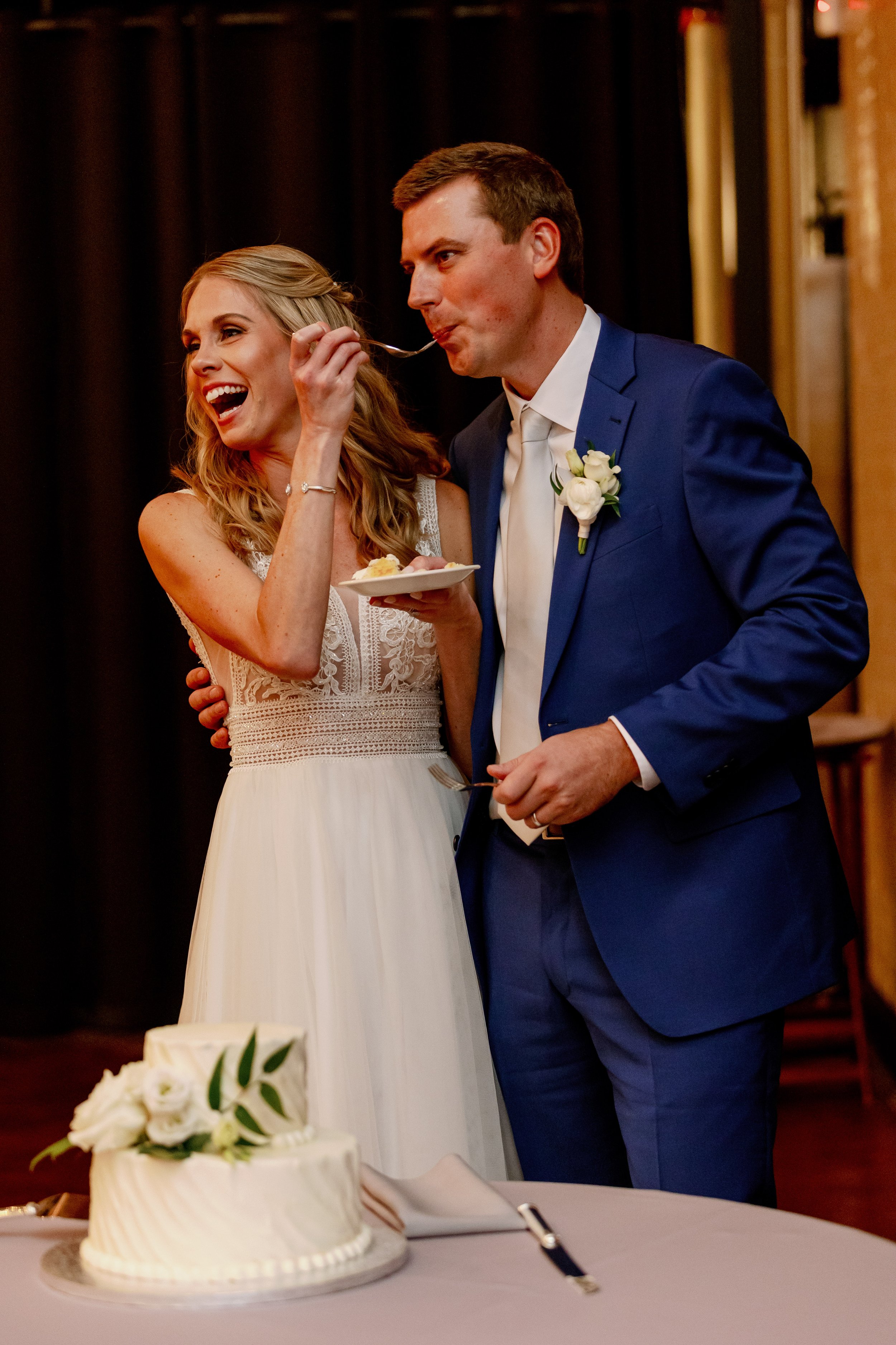 Bride and groom laugh together while cutting and sharing their wedding cake during the reception at Market Hall.