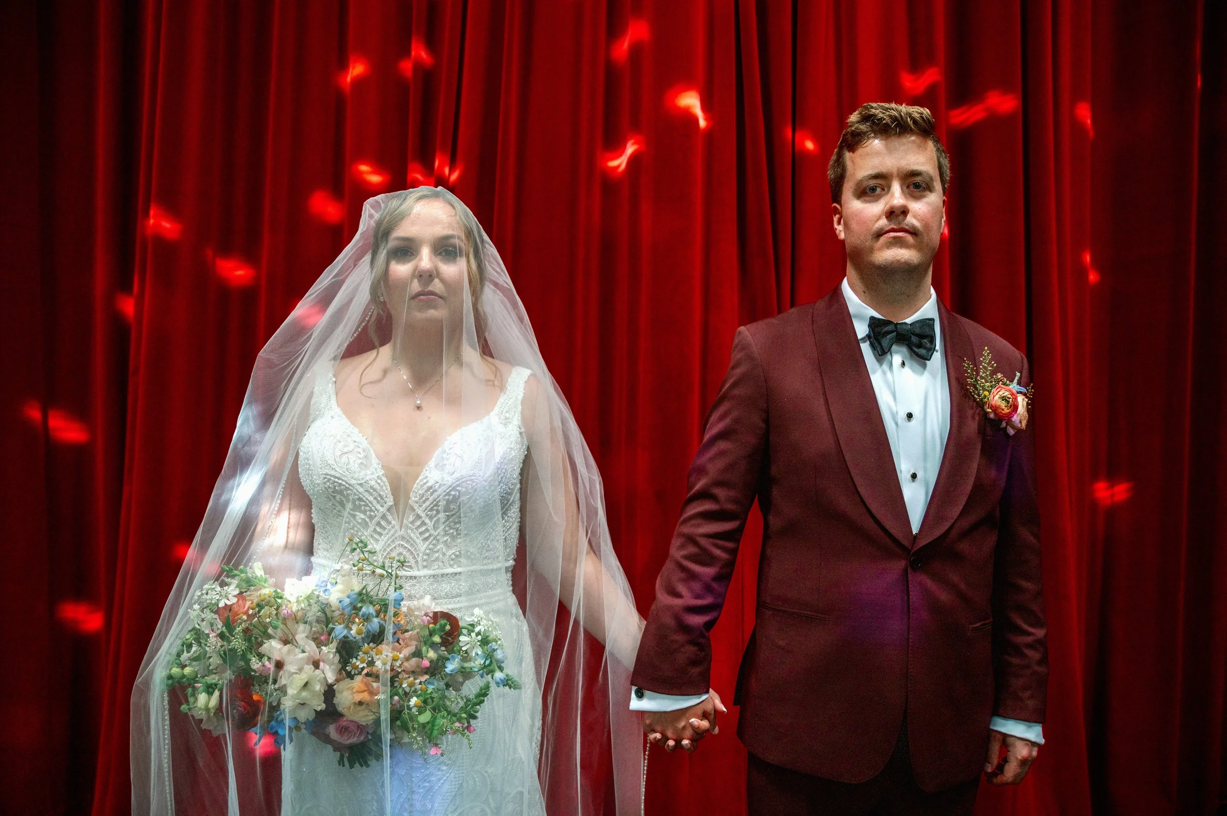  Bride and groom holding hands in front of red stage curtains at Haw River Ballroom wedding in Saxapahaw North Carolina 