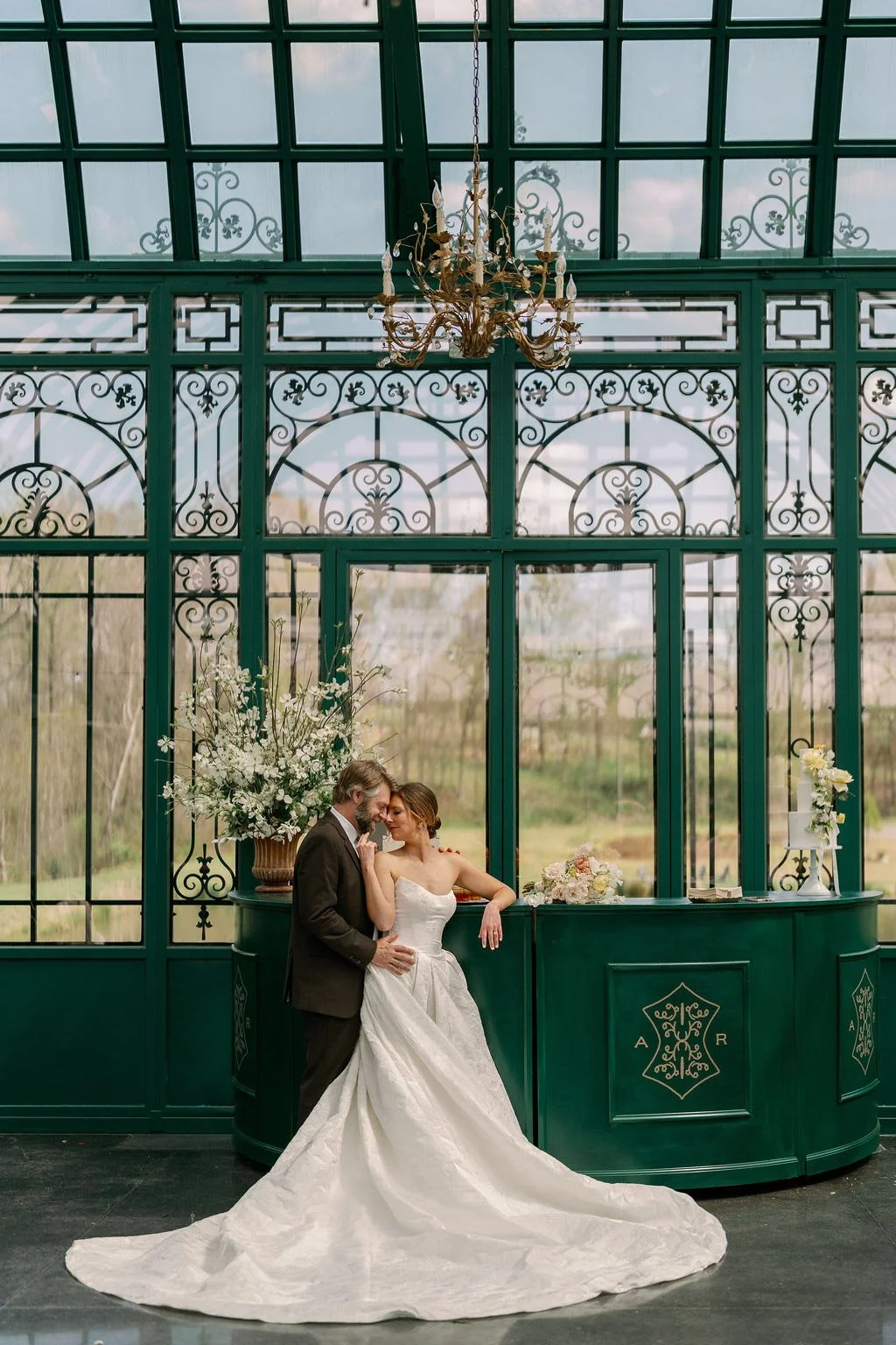  Couple embracing in front of the emerald glass and ironwork in the Solarium at The Little Chapel at Haven Ridge 