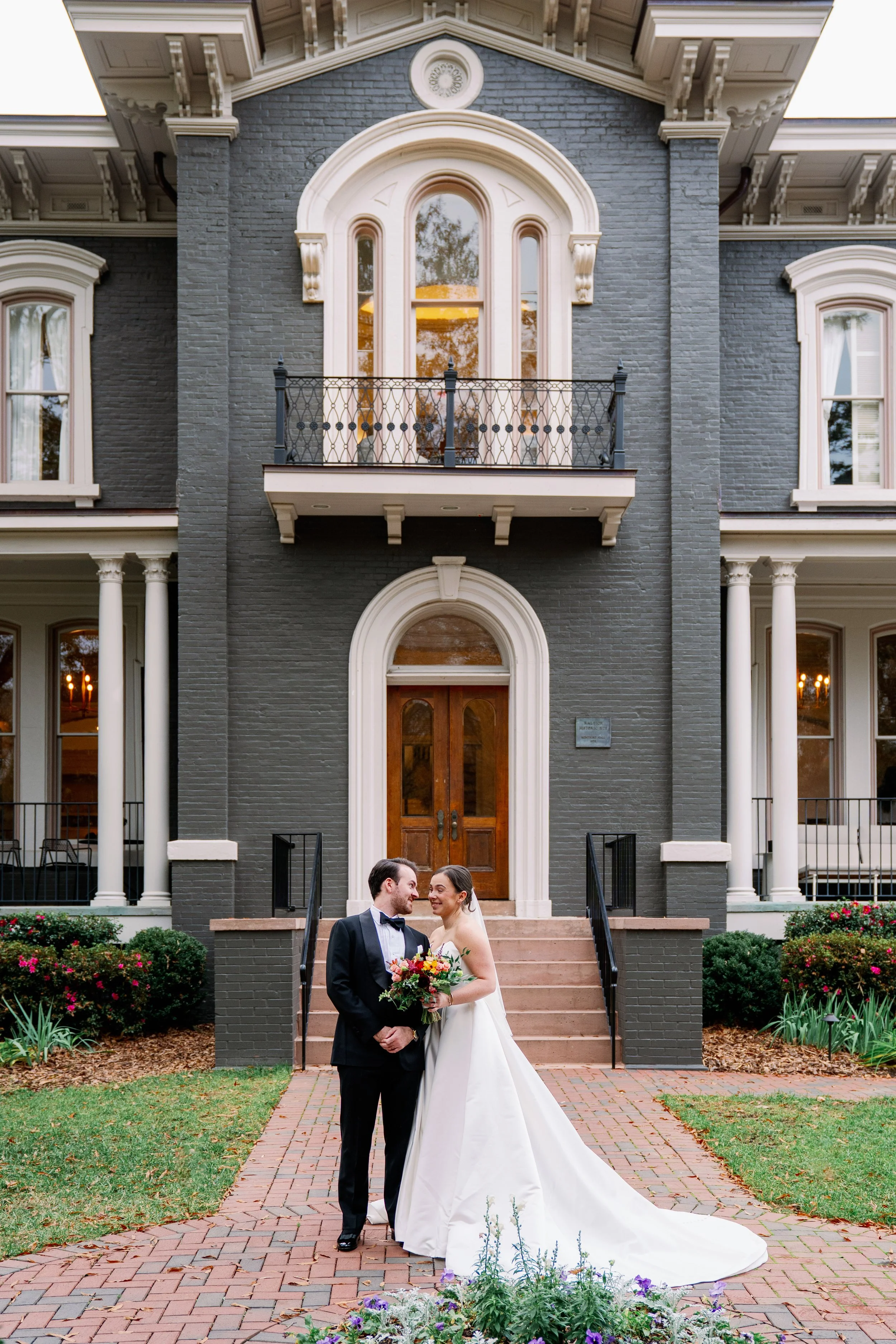  Bride and groom stand on the brick path in front of Heights House Hotel's Victorian facade in downtown Raleigh 