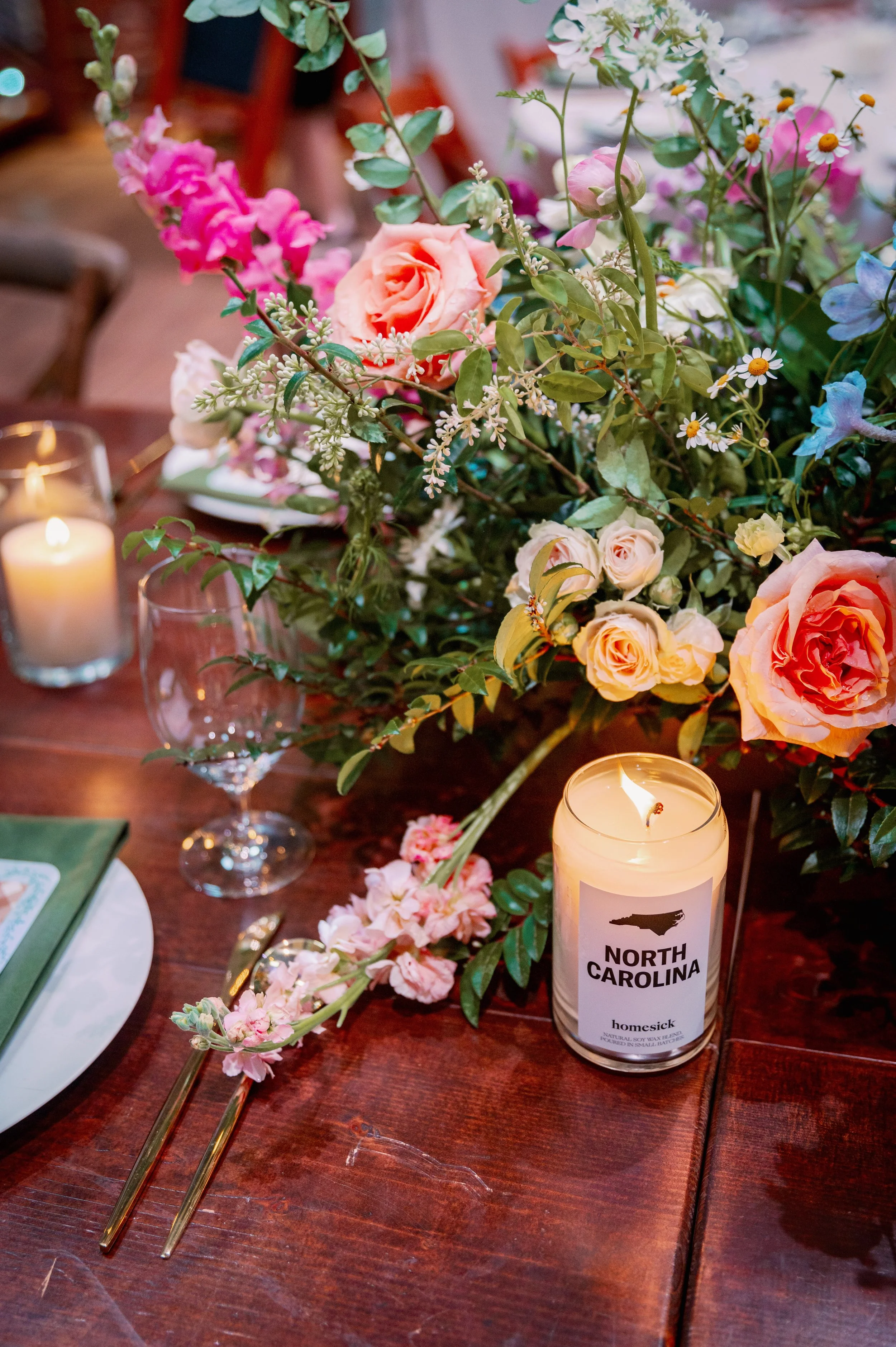 Colorful floral centerpiece and candle on a wooden reception table at a Haw River Ballroom wedding in Saxapahaw, North Carolina