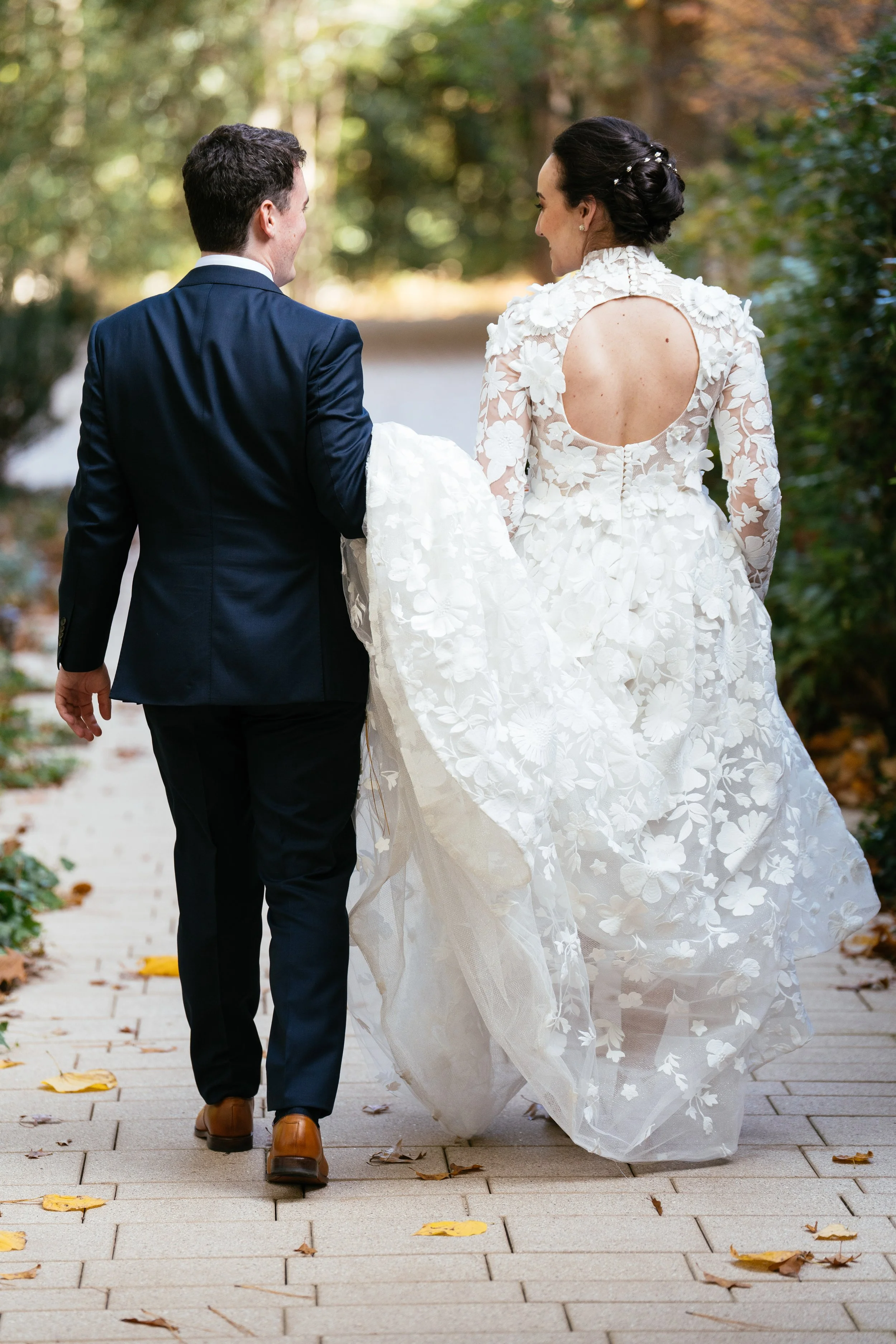 Bride and groom walking hand in hand during their fall wedding at The Umstead Hotel in Cary North Carolina, showcasing the back of the lace wedding dress and an intimate just married moment.