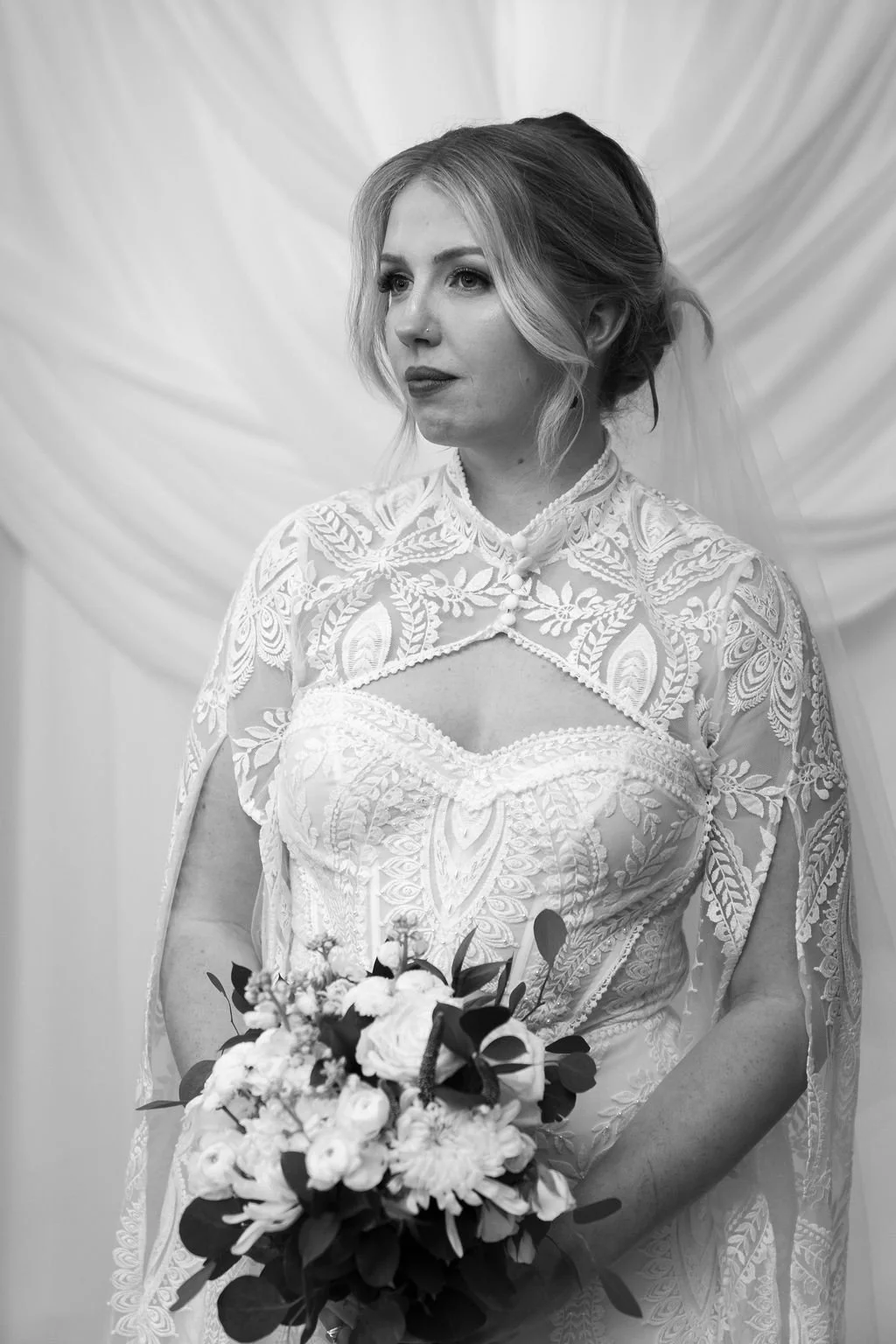 Black and white bridal portrait of bride wearing an intricate lace cape wedding gown with bouquet at a Winston Salem NC wedding