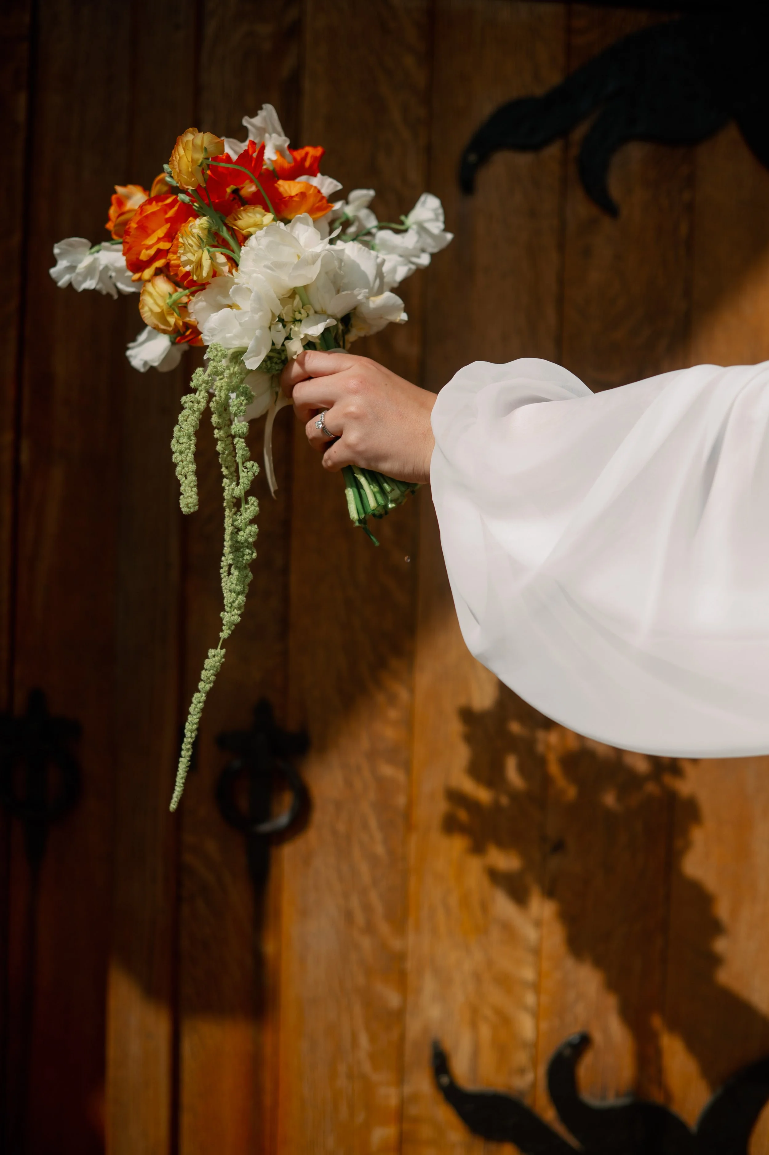 Person holding a bouquet of orange, white, and cream flowers in front of a wooden door with black decorative details.