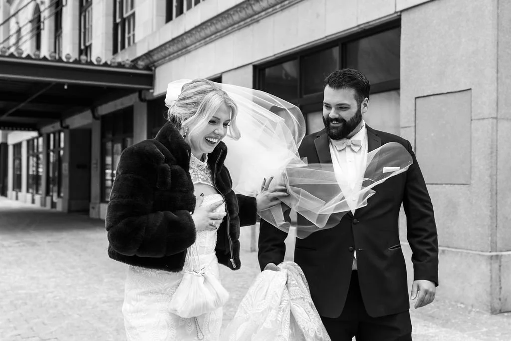 Bride laughing as her veil blows in the wind during outdoor wedding portraits on a downtown Raleigh street